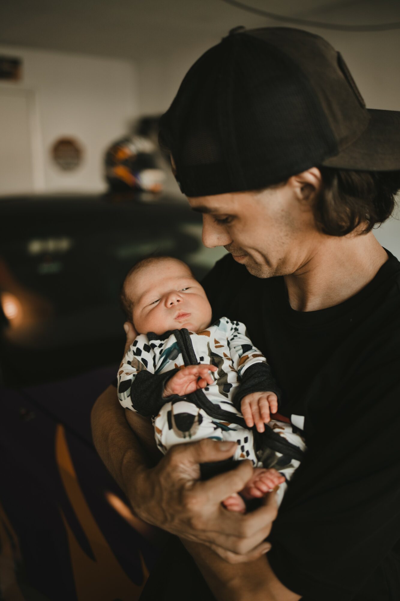 Person holding a sleeping baby indoors, looking down at the baby with a gentle expression.