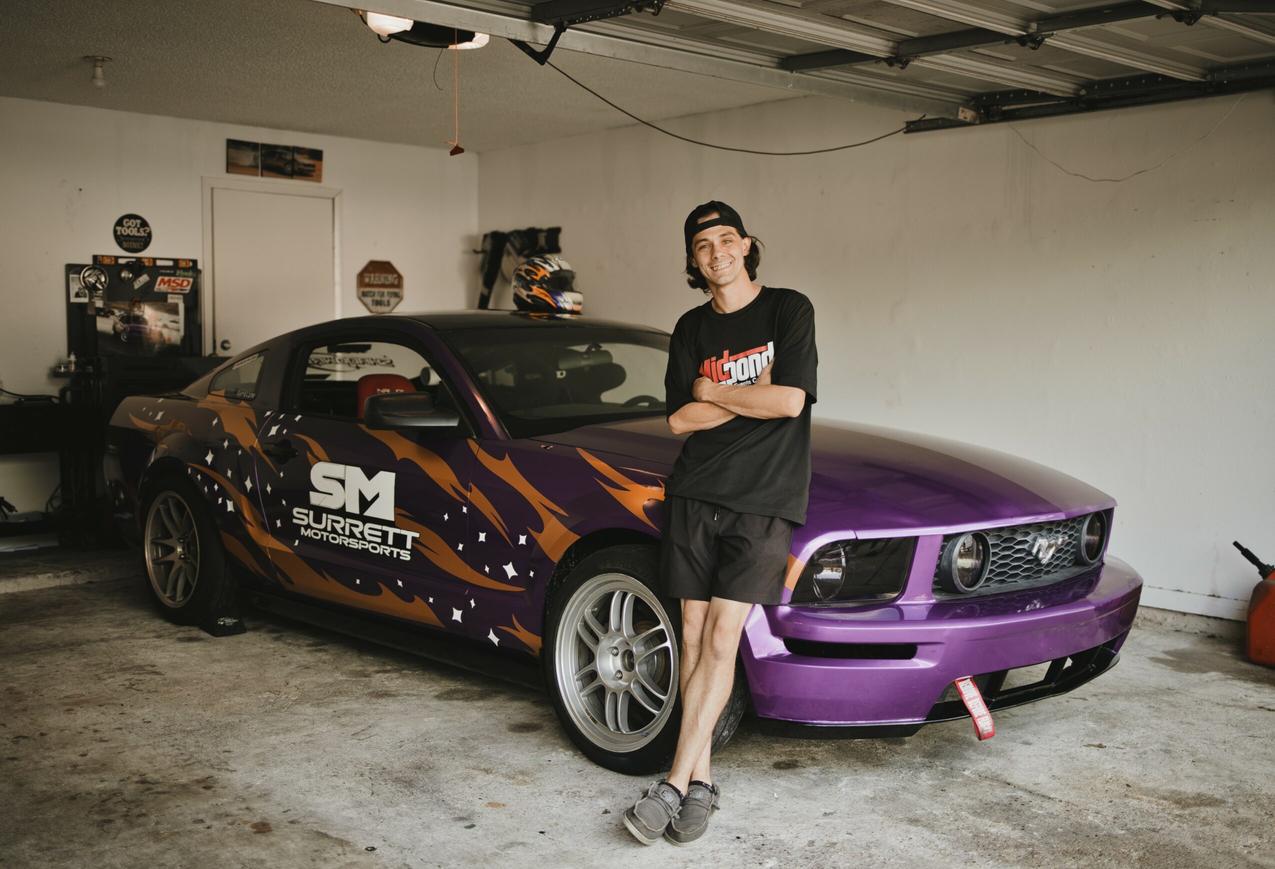 Person standing next to a purple and black sports car with a custom wrap in a garage.
