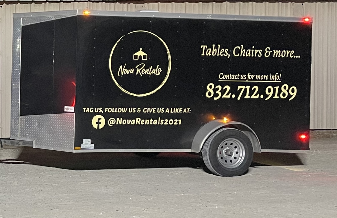 Black trailer with gold and white text advertising tables, chairs, and more, with contact information and social media handle.