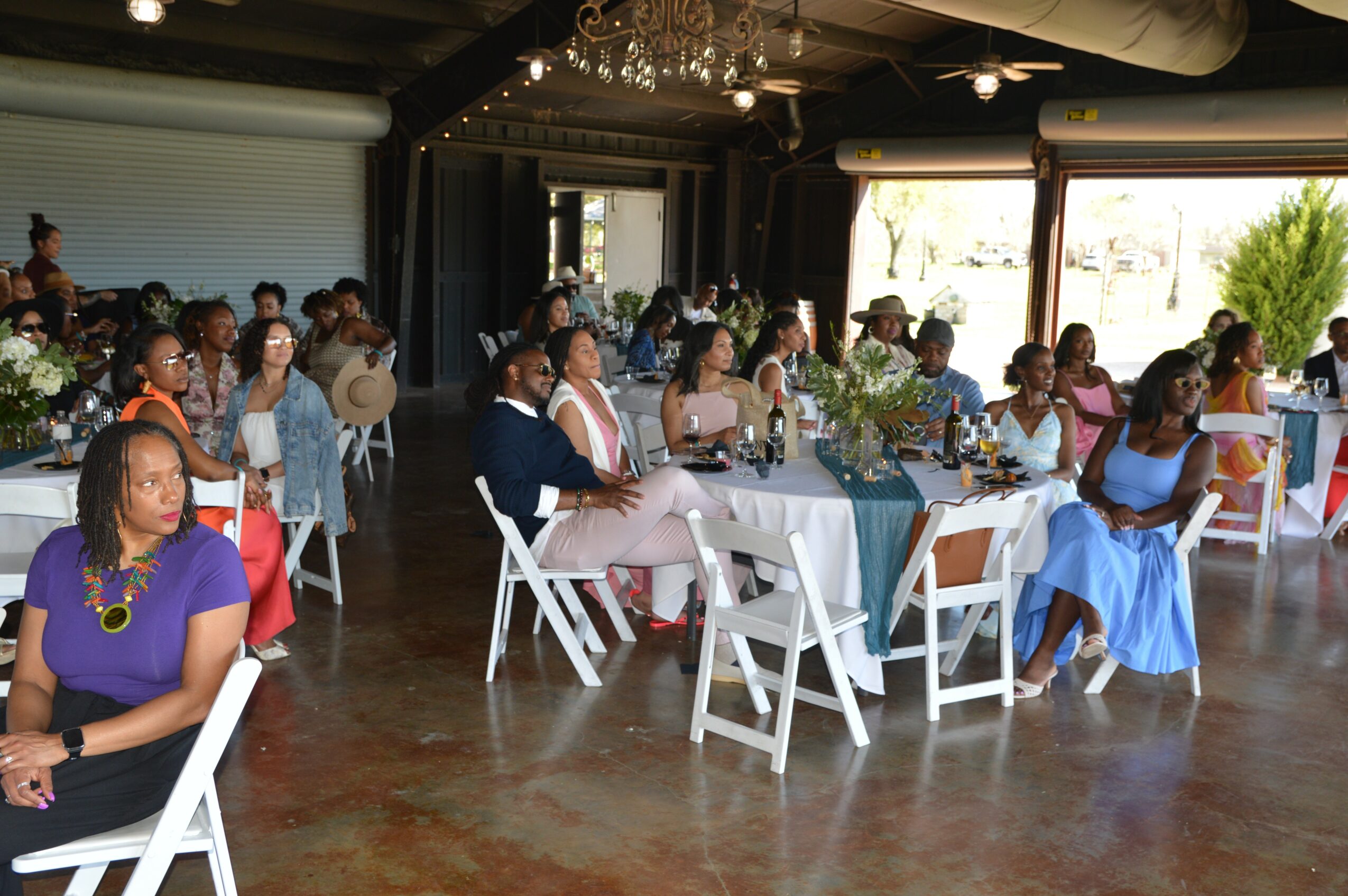 People seated at tables in a decorated indoor event space with large windows and natural light.