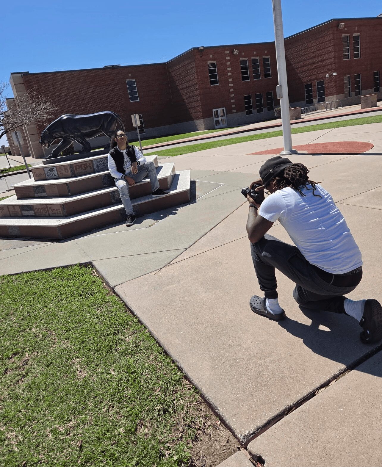 Person sitting on steps outdoors with a building in the background, photographer crouching taking a picture, sunny day.