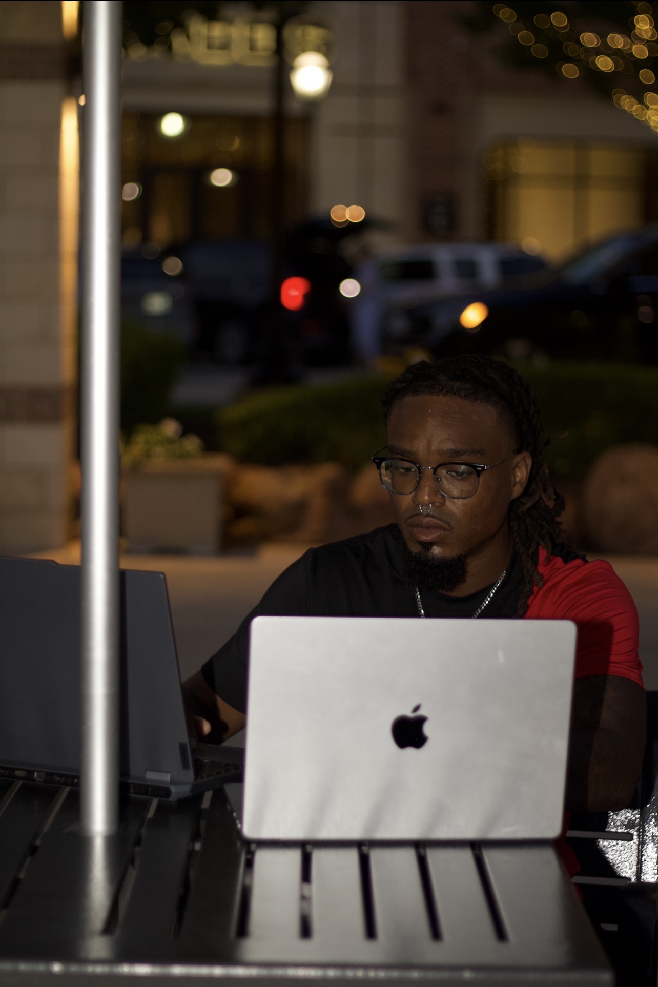 Person working on a laptop outdoors at night, with a blurred city background and streetlights.