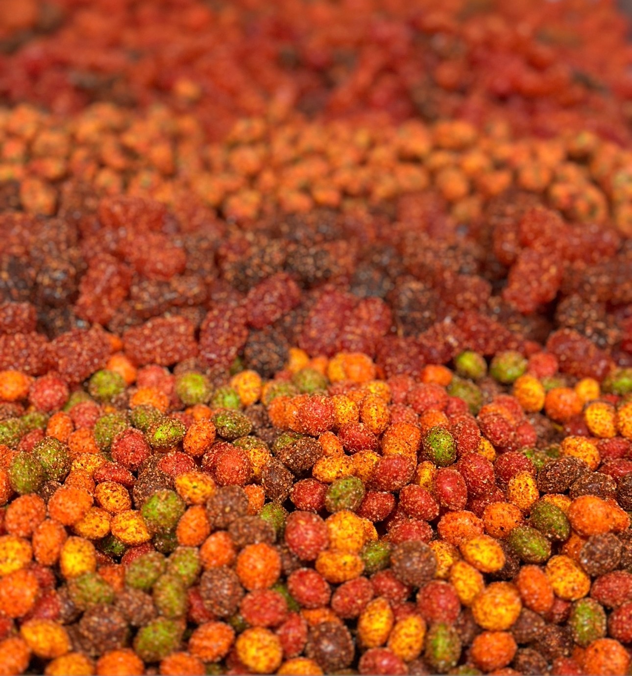 Close-up of colorful small round objects, mostly red, orange, green, and brown, scattered across a surface.