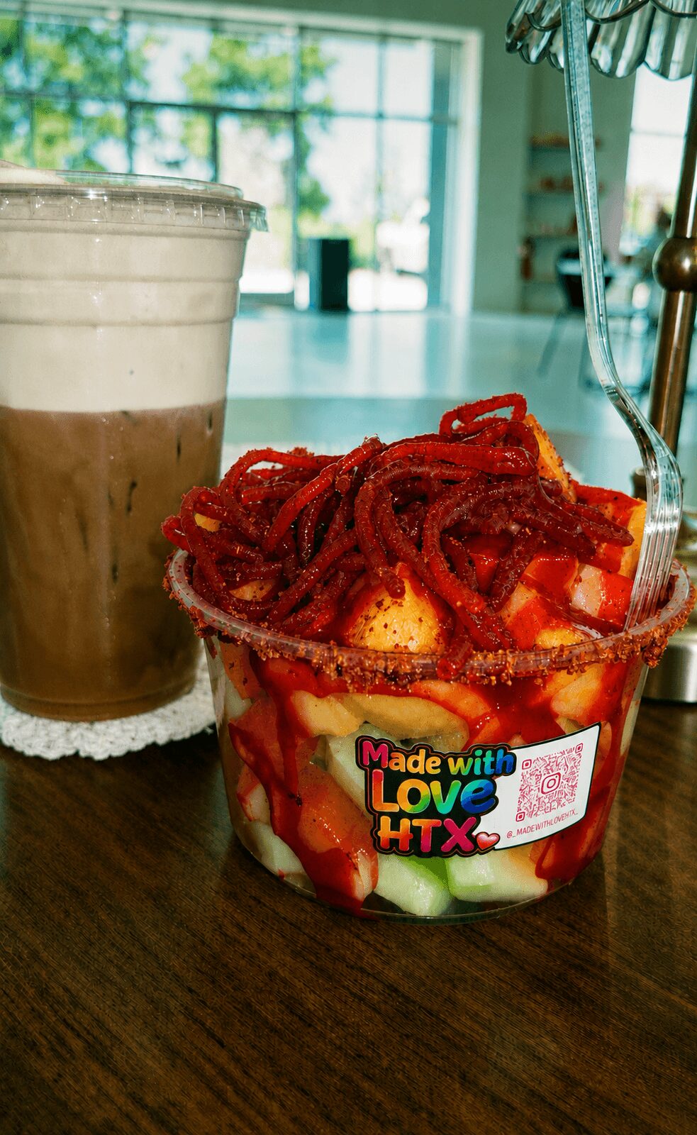 Strawberry and cucumber salad with red pasta and a cold beverage in a glass, on a wooden table, with a window in the background.