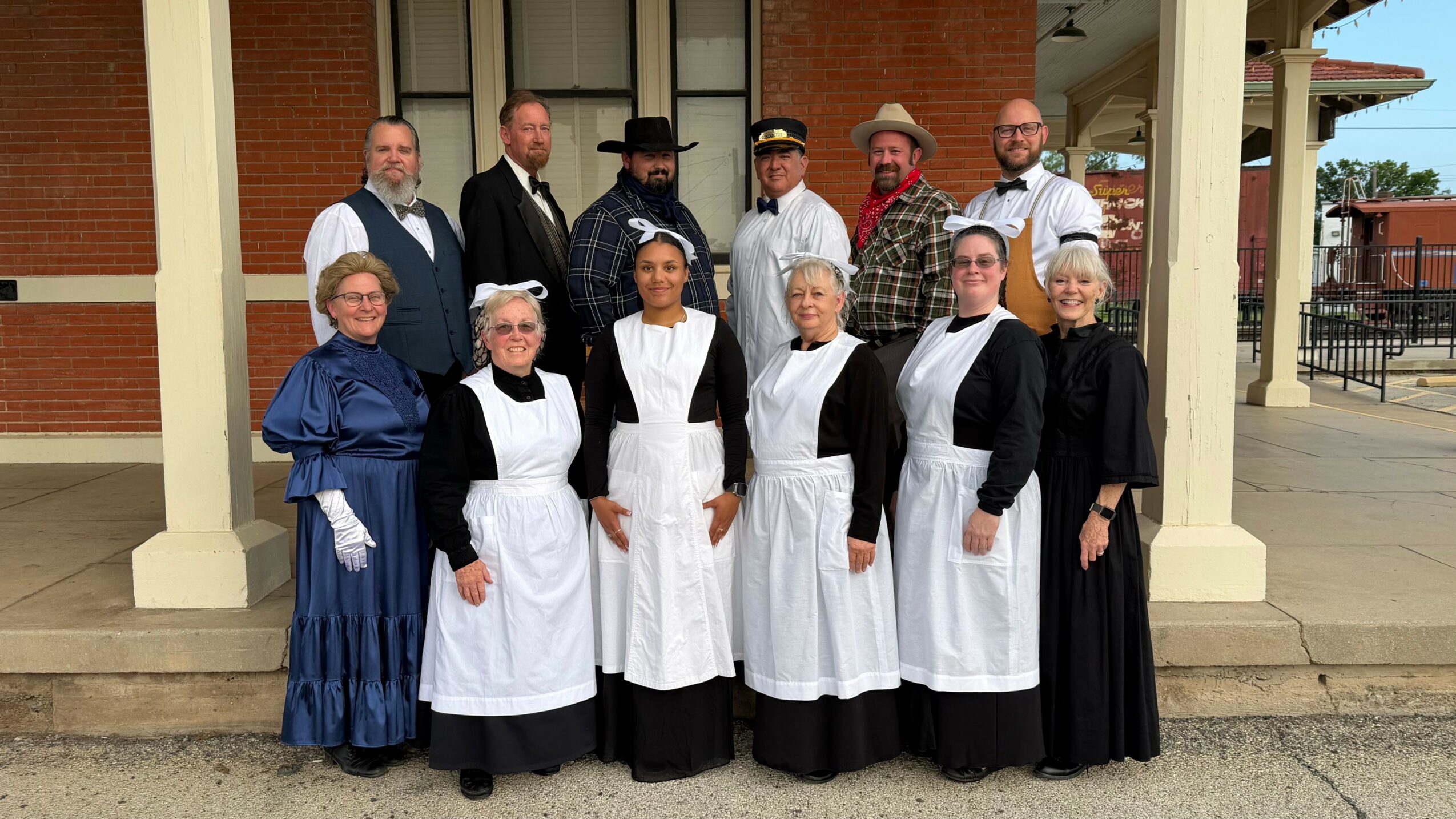 Group of ten people, some in historical costumes, standing outside a building with columns, posing for a photo.