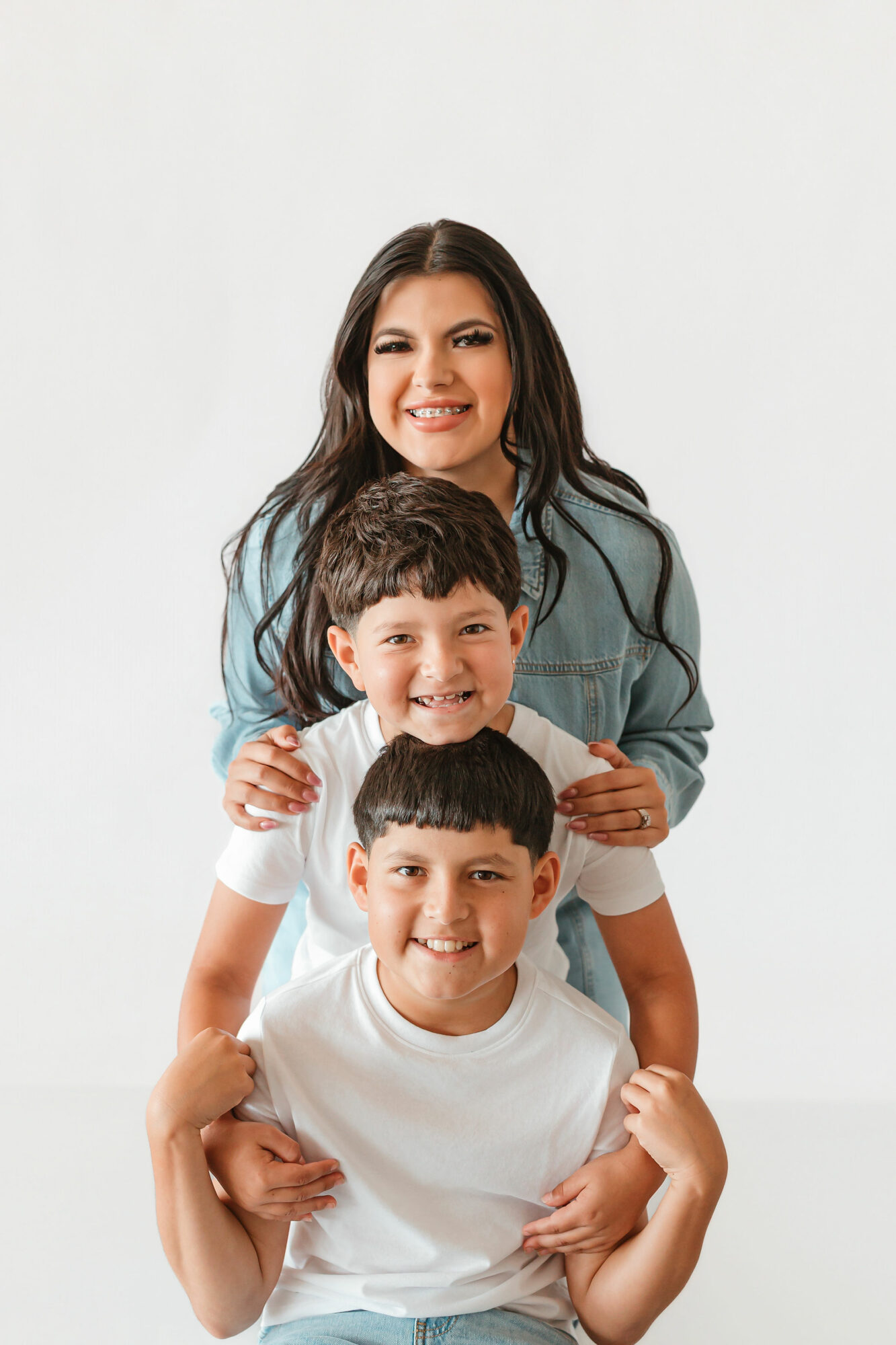A woman with two young boys smiling, standing against a plain white background.