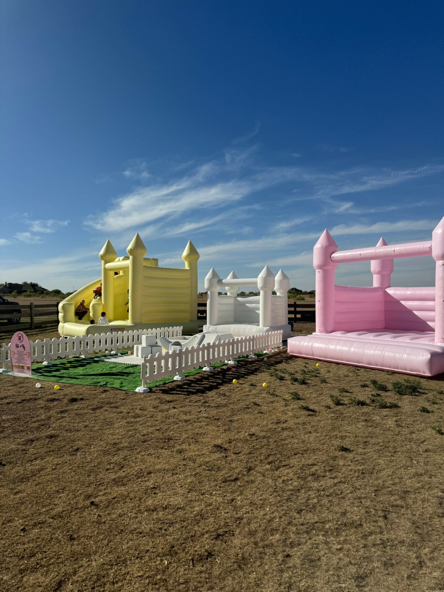 Colorful inflatable castles in yellow, white, and pink, set on a grassy area under a blue sky with clouds.