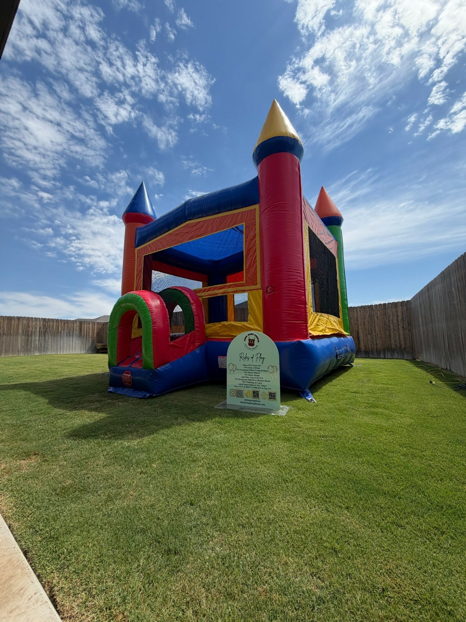 Colorful inflatable bounce house shaped like a castle with red, blue, yellow, and green sections, set on a grassy yard under a partly cloudy sky.