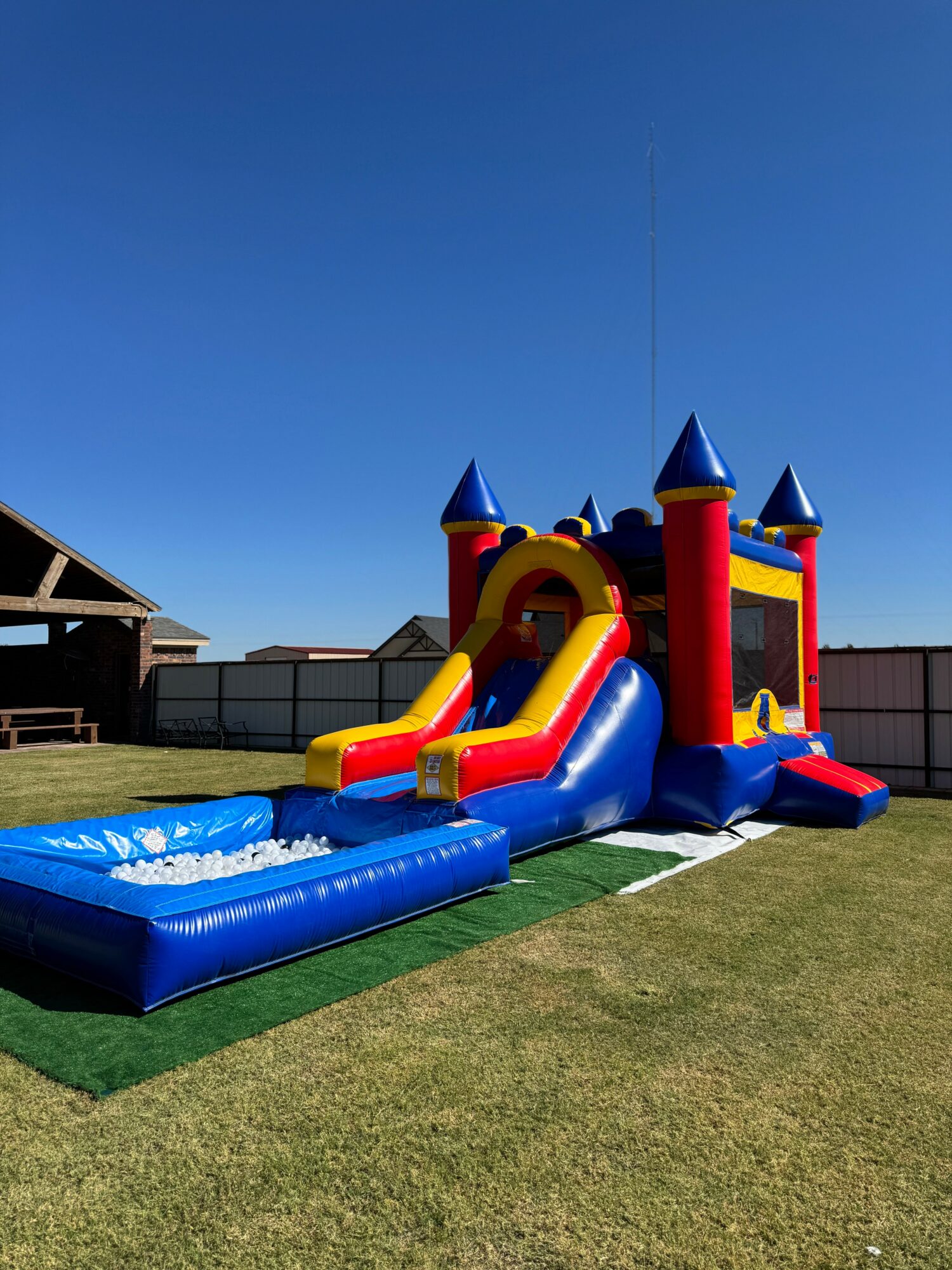 Colorful inflatable castle with slide and water feature on a grassy yard under a clear blue sky.