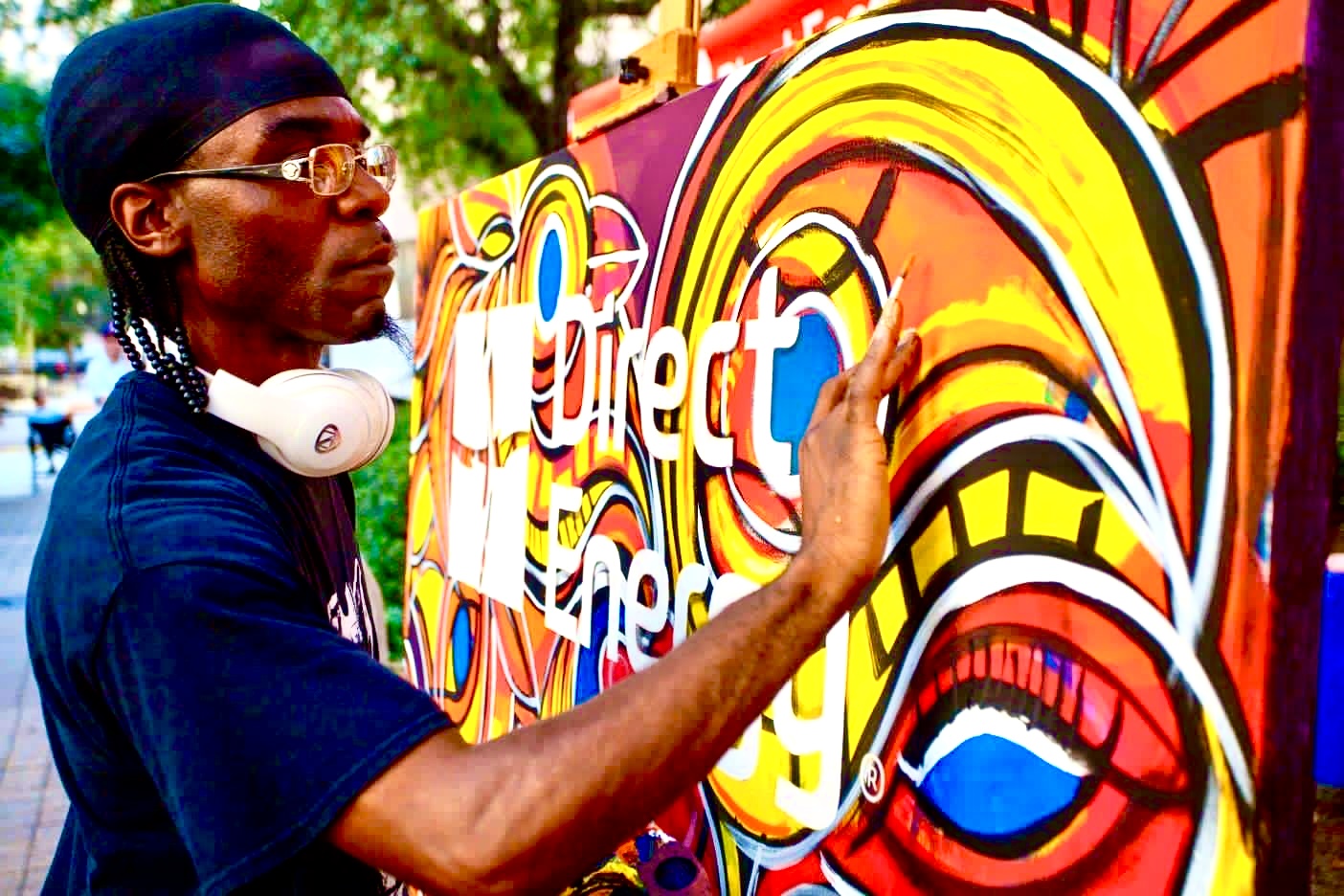 Person painting colorful graffiti on a wall outdoors, wearing glasses and headphones around neck.