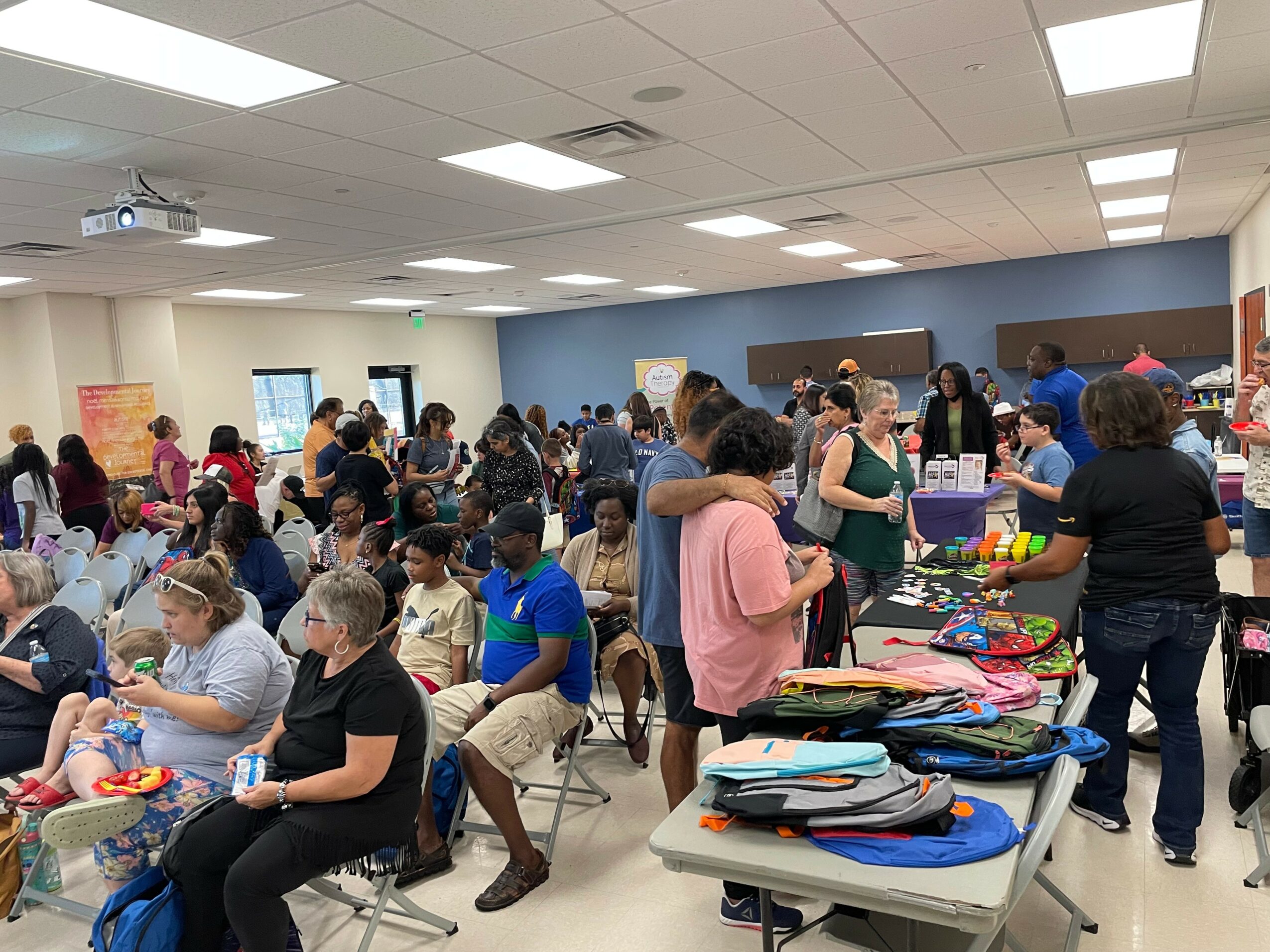 Crowd of children and adults in a room with tables and displays, engaging in activities and conversations.