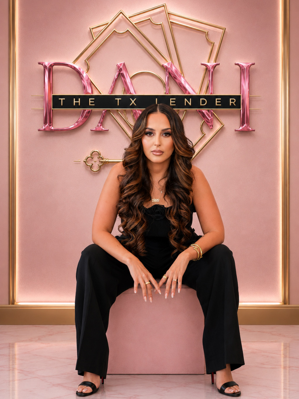 Woman with long wavy hair in black outfit sitting on pink ottoman in front of a pink background with neon sign.