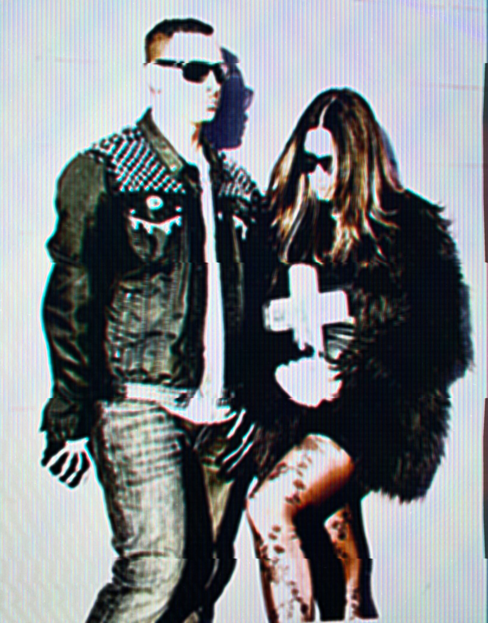 Two people wearing sunglasses, one holding a cross, standing against a plain background.
