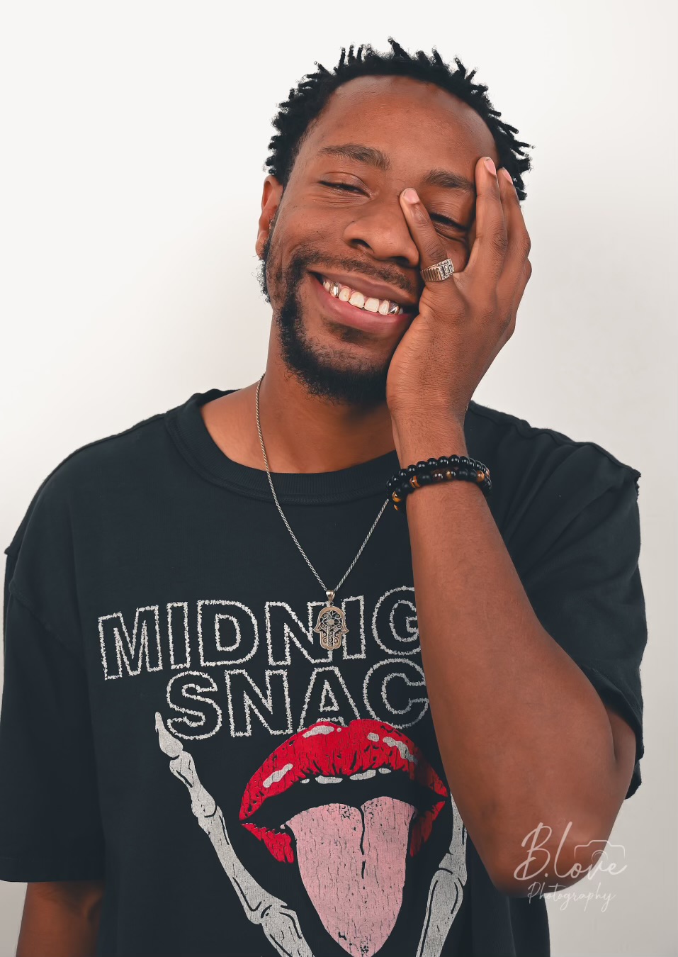 Person smiling with eyes closed, hand covering part of face, wearing a black T-shirt with graphic design, against a white background.