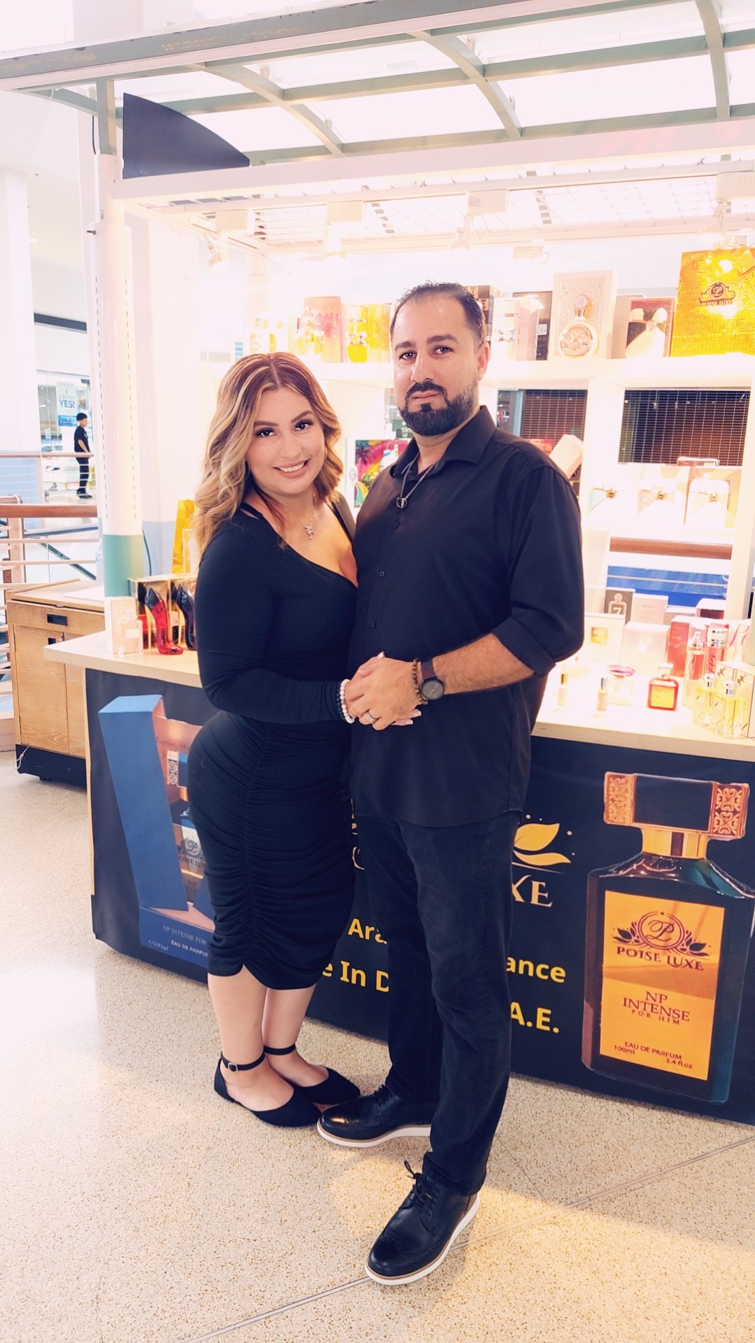 Two people standing together in a store, holding hands, smiling, with shelves and products in the background.