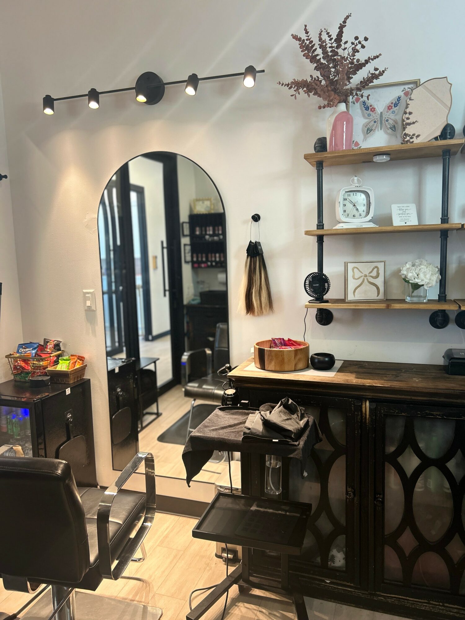 Interior of a room with a mirror, shelves with decorative items, a bar counter, and a chair, illuminated by a ceiling light.
