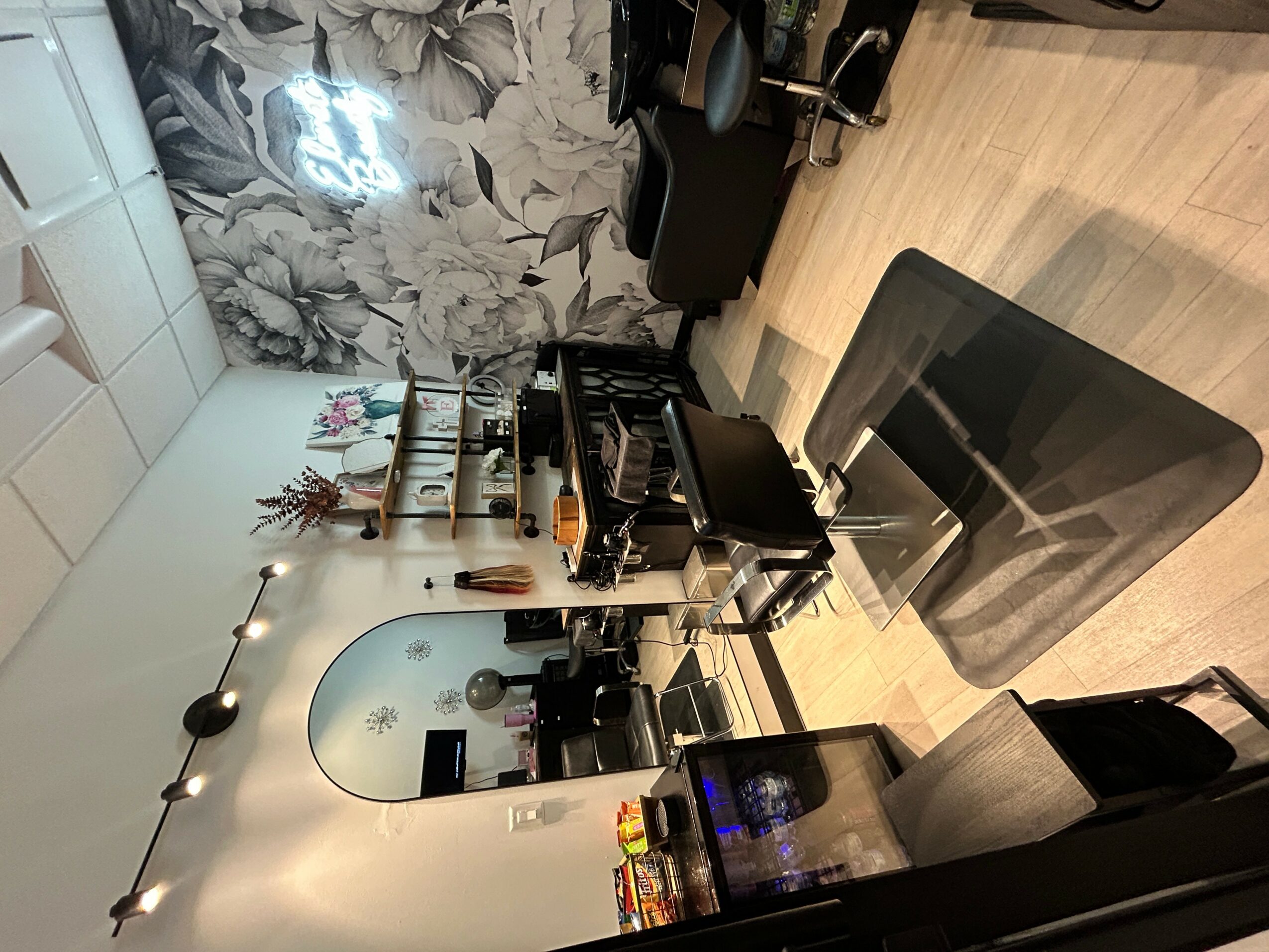 Room with a wall mirror, floral wallpaper, and a workspace with a computer, desk, and various items.