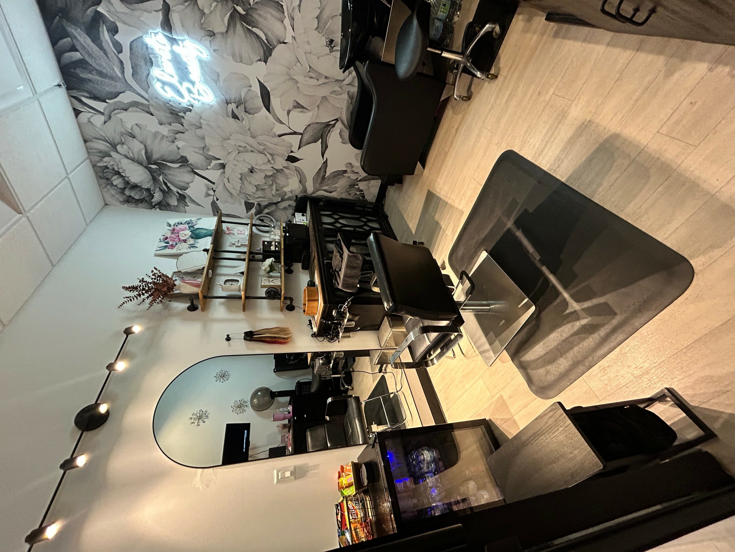 Room with a mirror, makeup items, and a black chair on a wooden floor.