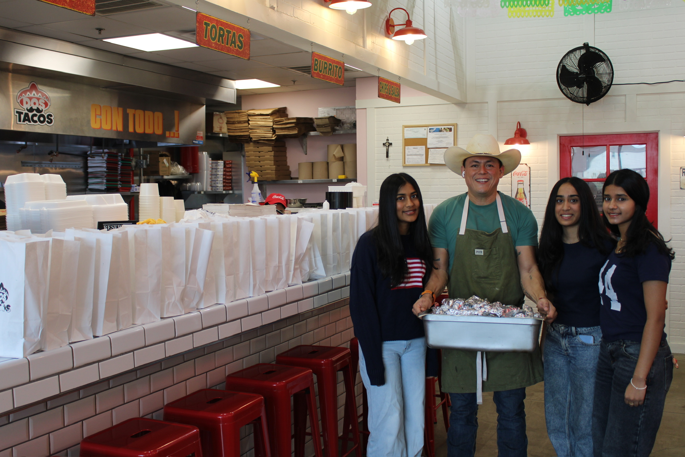 Four people standing inside a restaurant, with a counter and food packages behind them, smiling at the camera.