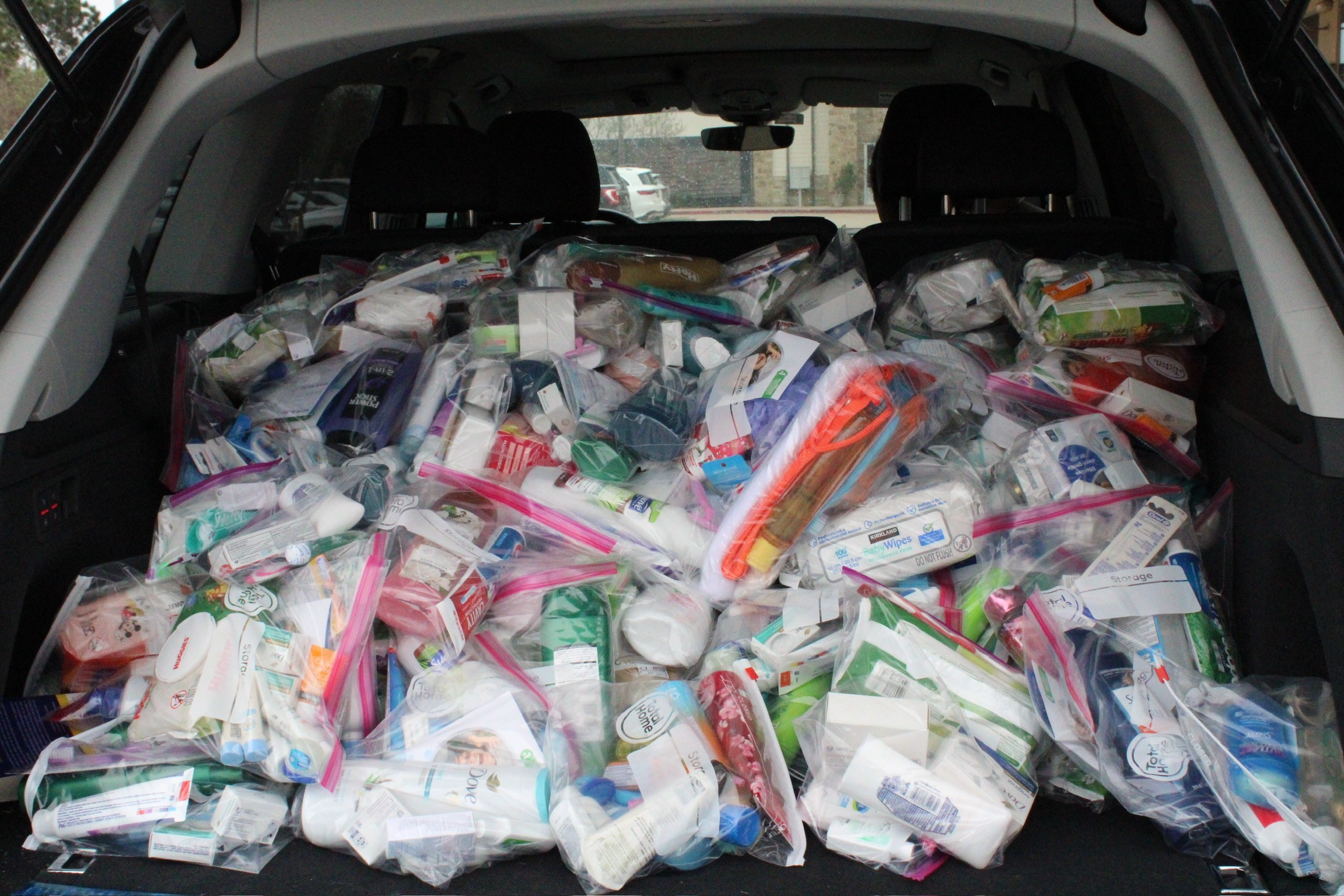 Car trunk filled with numerous sealed plastic bags containing various toiletries and personal care items.