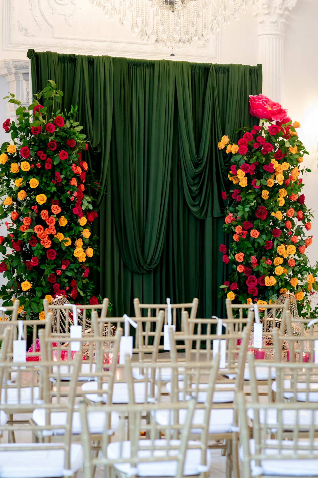 Green curtain with floral arrangements on each side, chairs arranged in front, in a decorated indoor setting.