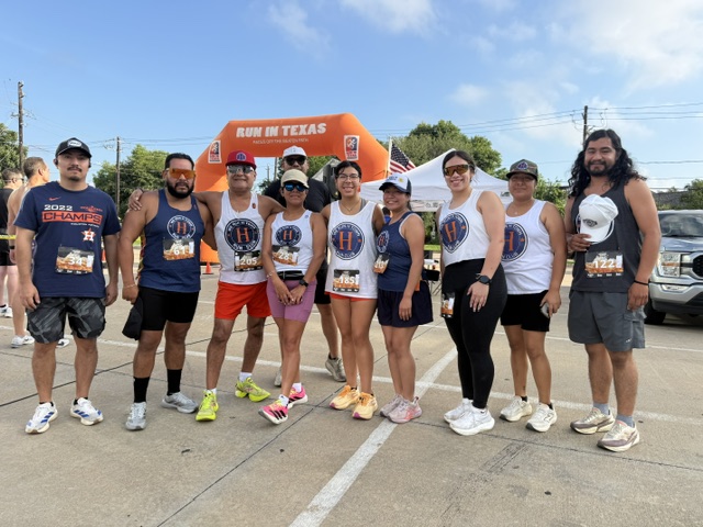 Group of ten people standing outdoors in front of an orange tent, wearing casual athletic clothing and hats.