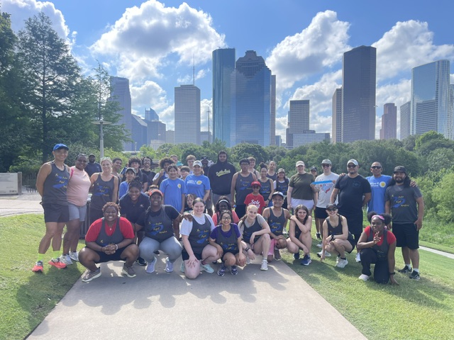 Group of people outdoors on a sunny day with city skyline and trees in background.