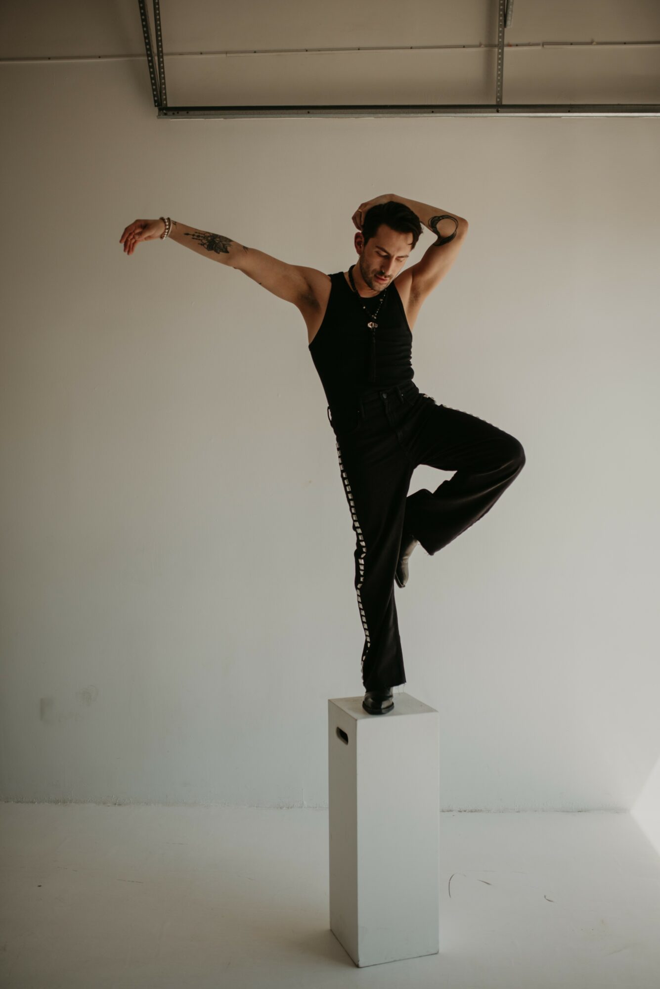 Person balancing on a white pedestal with one leg raised, arms extended, in a studio setting.
