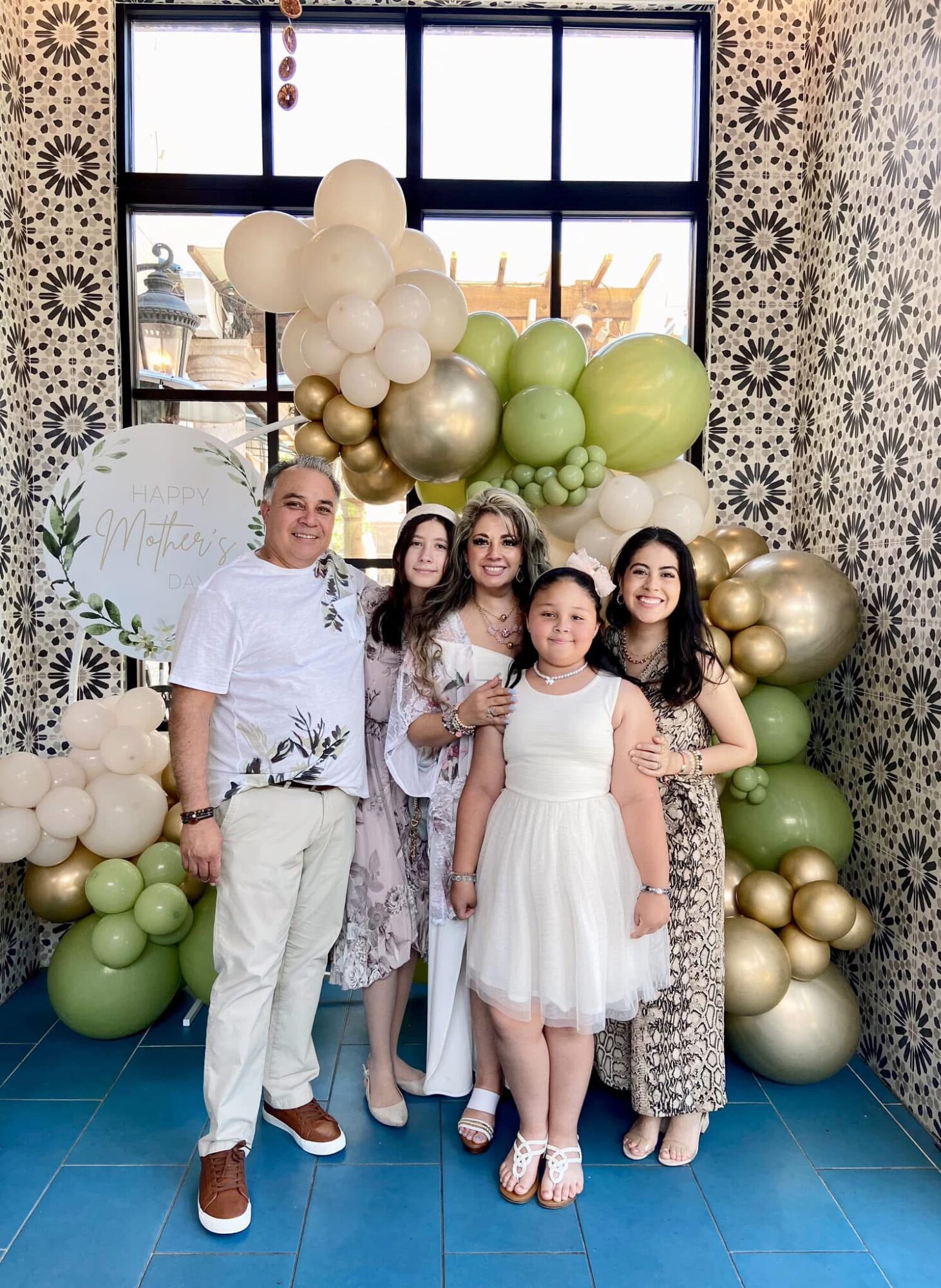 Group of five people, including children and an adult, standing in front of balloon decorations and a window, smiling.