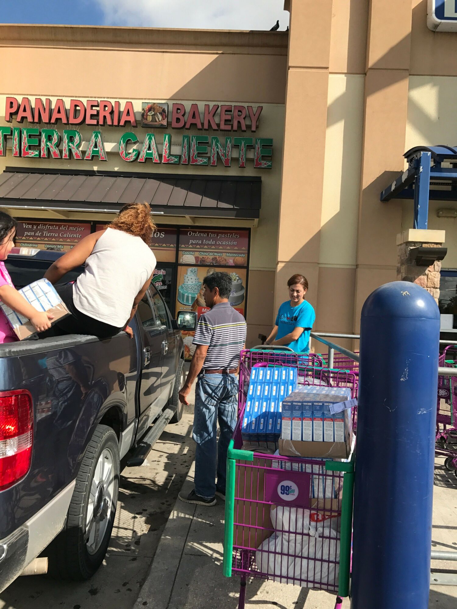 People shopping at a grocery store entrance with shopping carts outside a building, sunlight, and shadows.