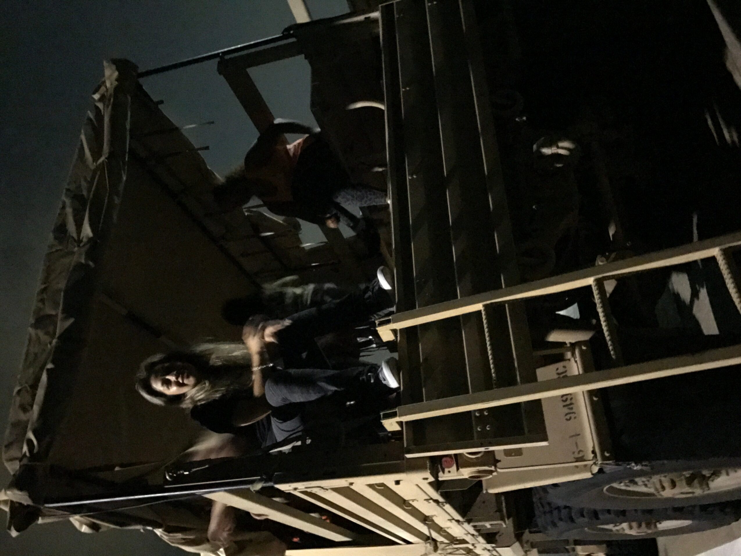 People are on a dark staircase with a railing, some sitting and some standing, in a dimly lit environment.
