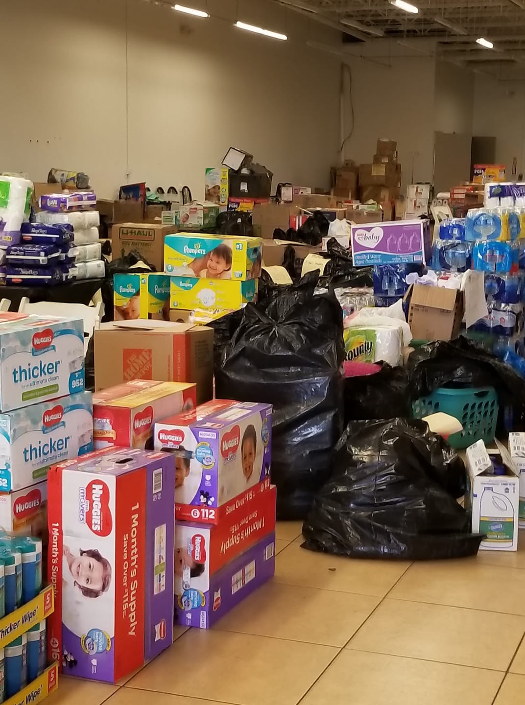 Warehouse with boxes and bags of supplies, some stacked, in a large room with high ceiling and fluorescent lights.