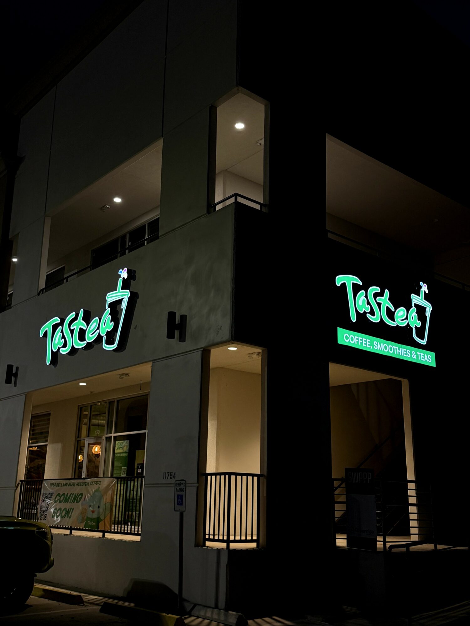 Night view of a building with illuminated signs reading 'Tasted' and a logo, with dark surroundings and interior lighting visible.