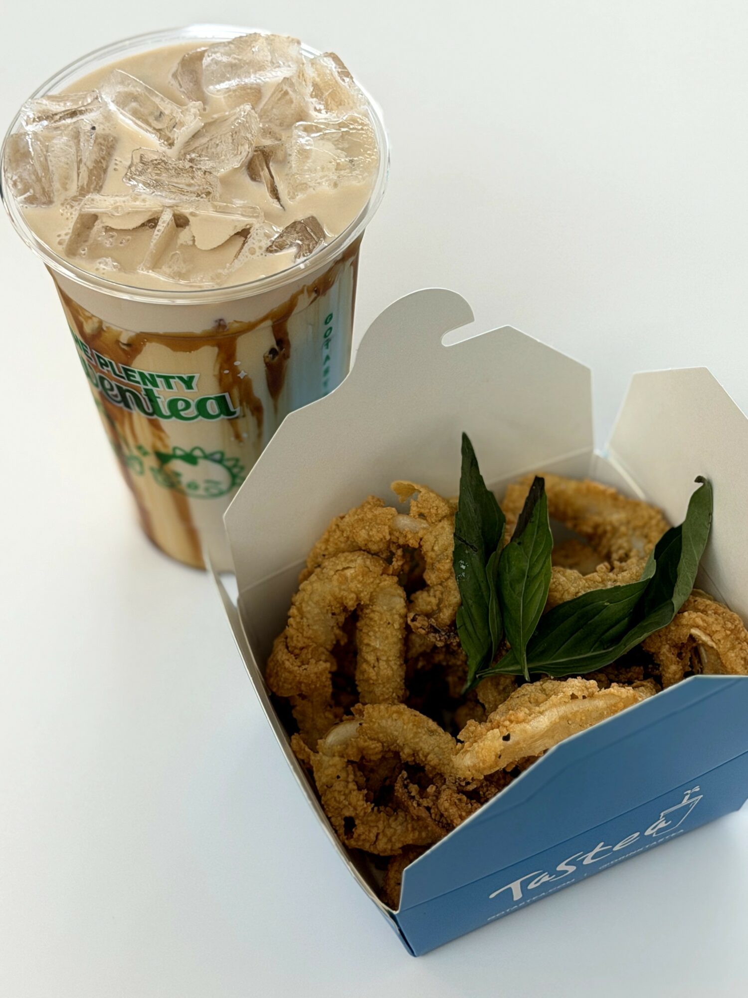 A cup of iced coffee with ice cubes and a side of fried chicken pieces with green garnish in a blue container.