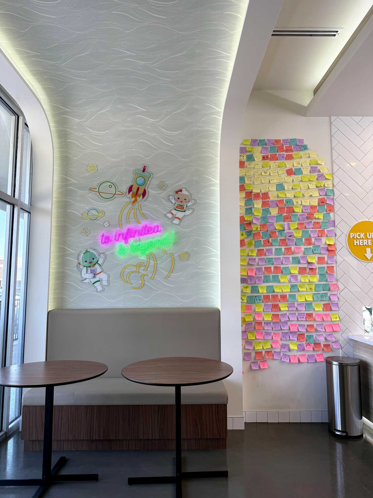 Interior of a modern space with a wall decorated with colorful sticky notes, a window, and a seating area with two round tables.