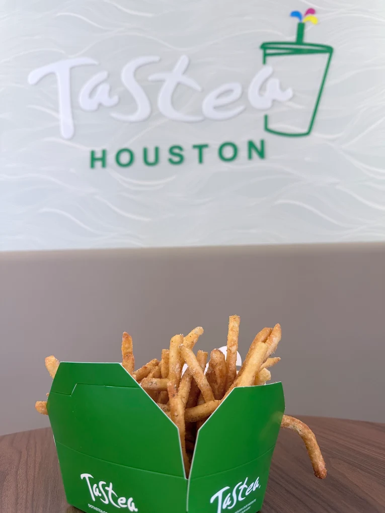 Green container of French fries in front of a wall with a logo reading 'Tasteea Houston' and a stylized drink with a straw.