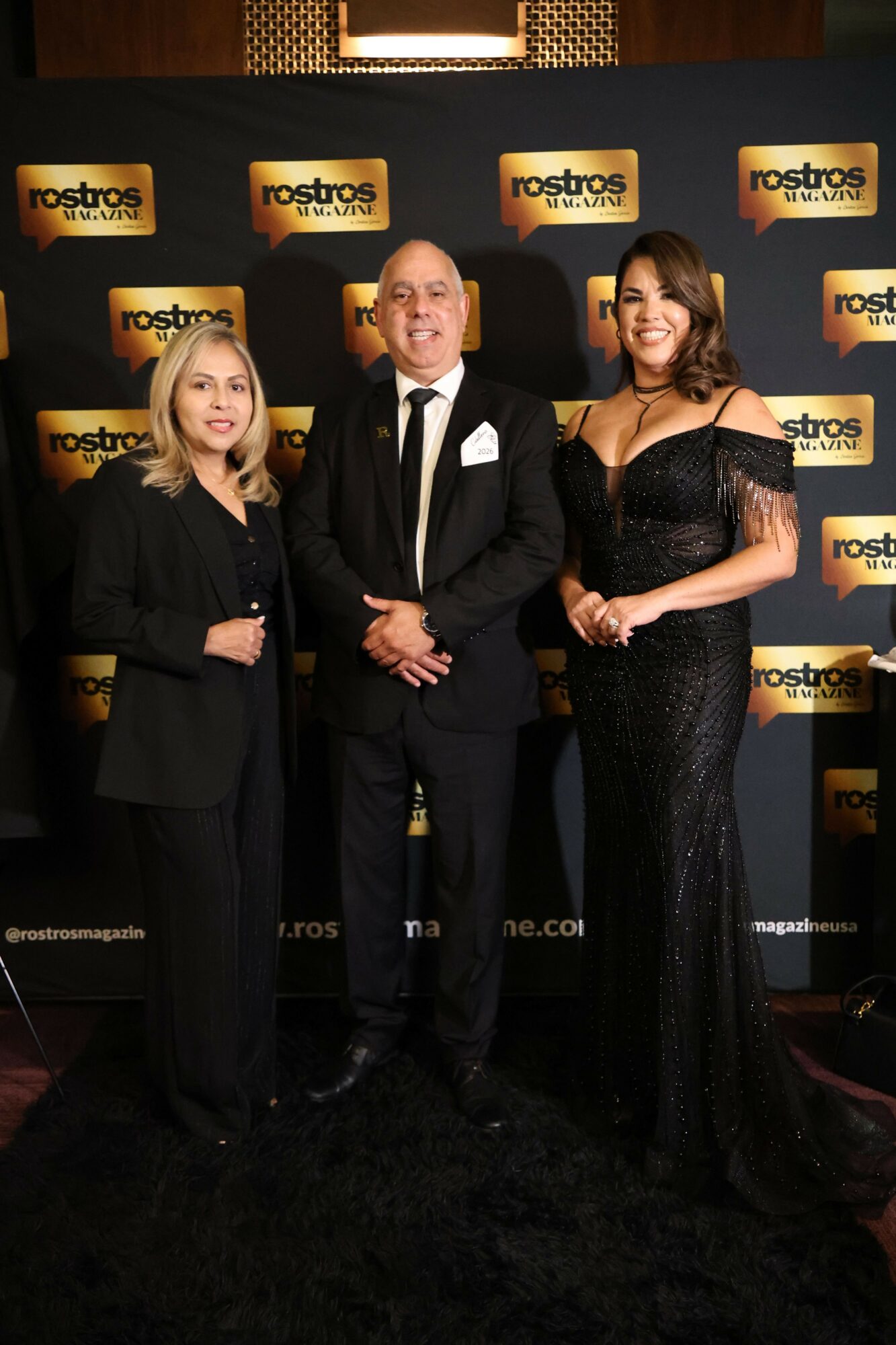 Two people shaking hands in front of a backdrop with logos, one woman and one man, both dressed in black.