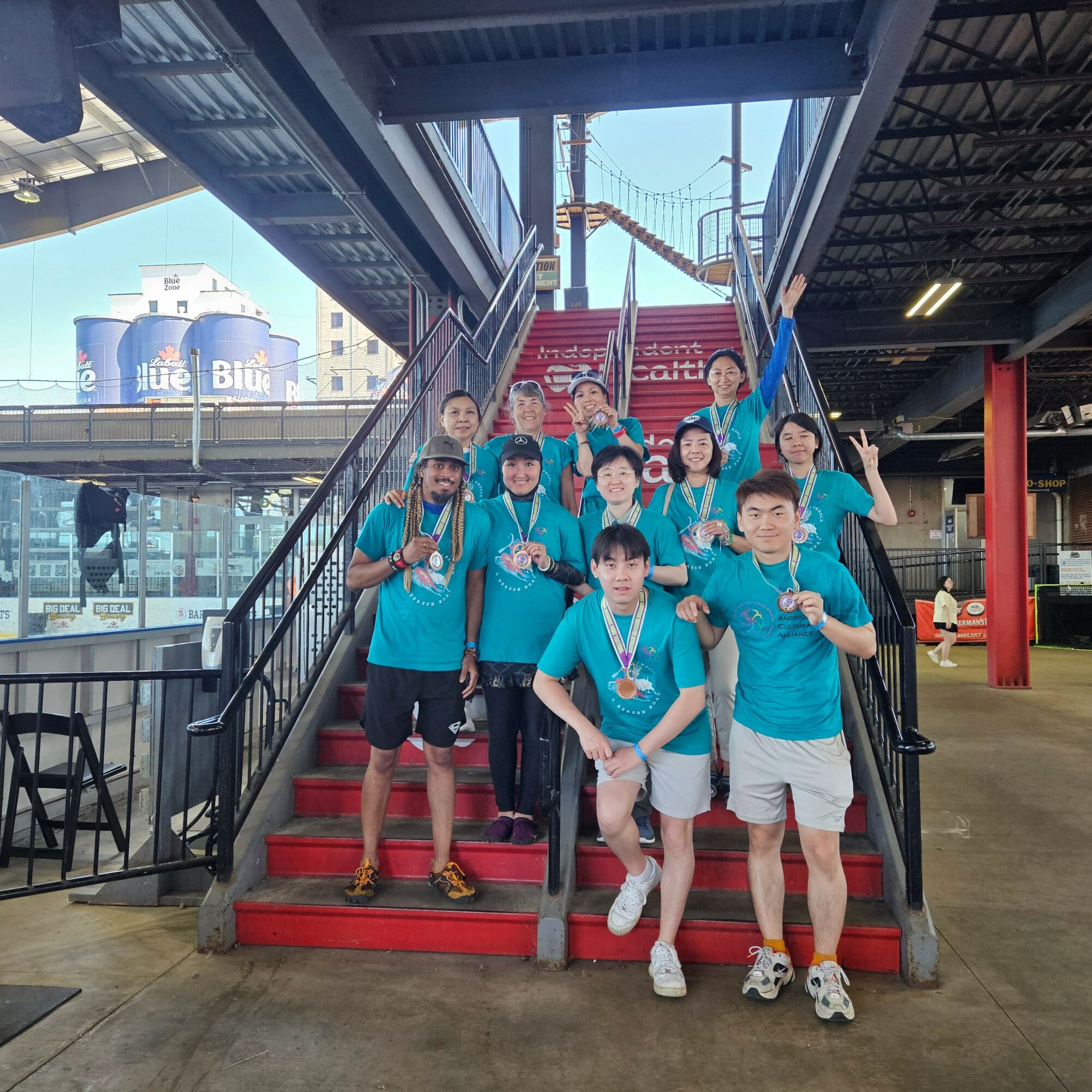 Group of people wearing blue shirts and medals standing on a red staircase inside a building, some making peace signs.