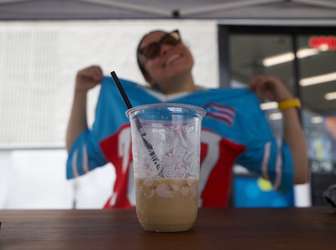 Person in a blue sports jersey holding it up, with a partially filled iced drink on a table in front, smiling.