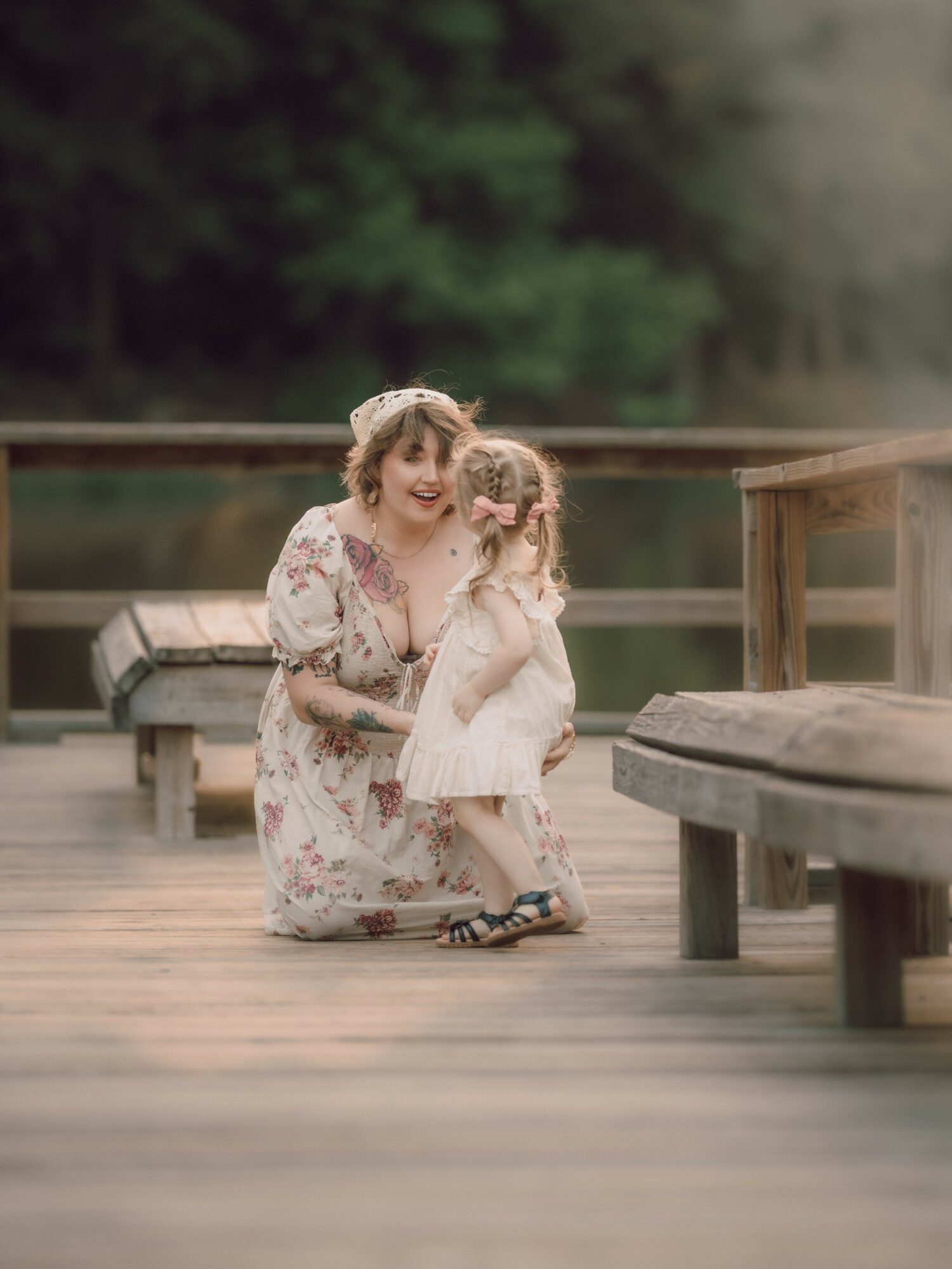 Woman and young girl hugging on a wooden dock with trees in the background.