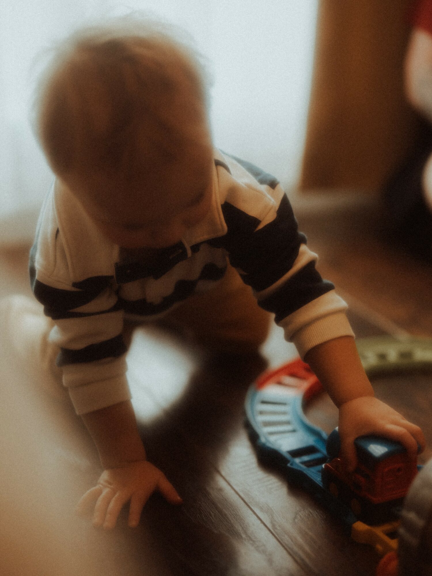 Child crawling on wooden floor playing with a toy train, wearing a striped shirt.