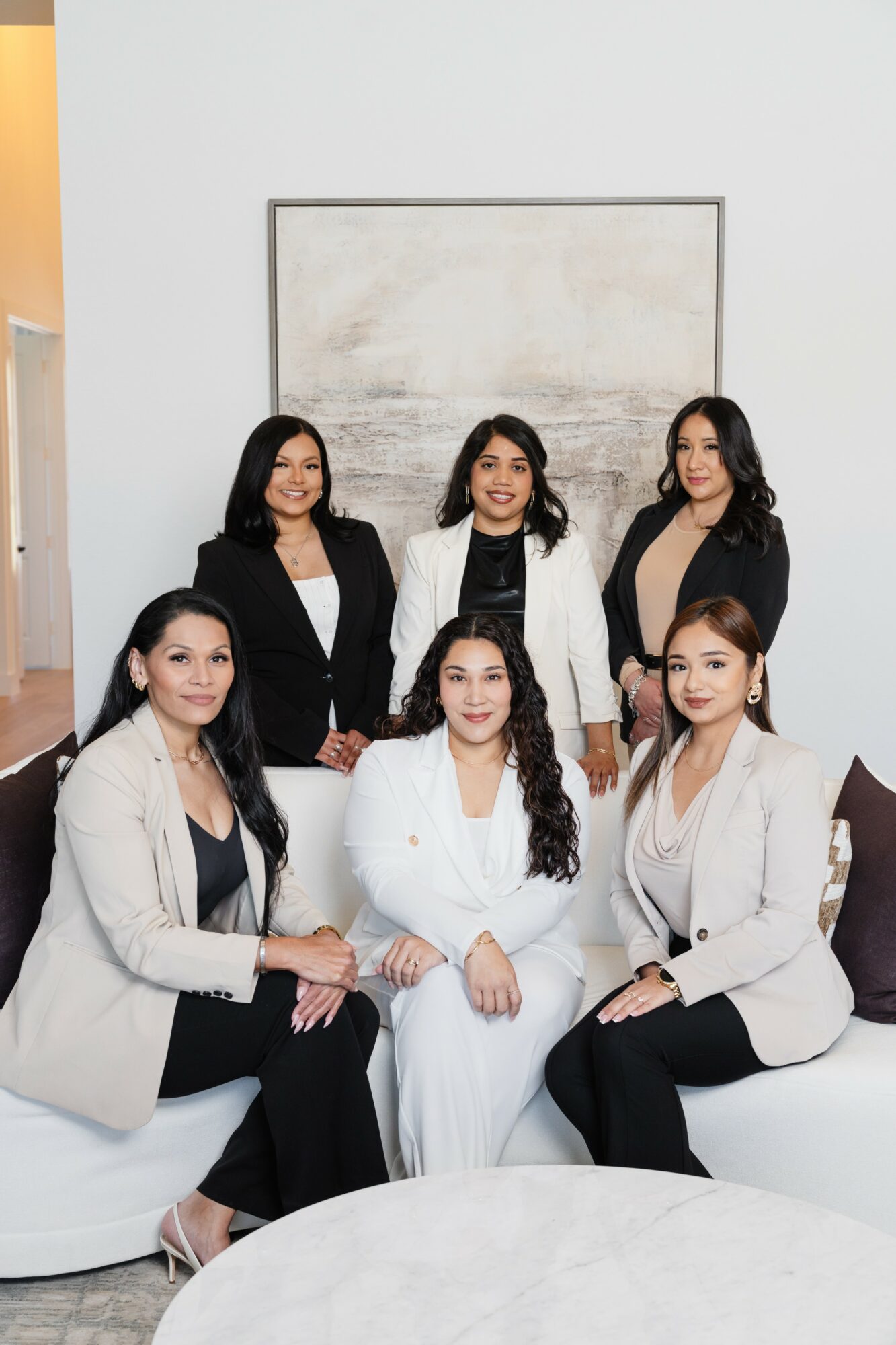 Six women in professional attire pose in a room with a large abstract painting on the wall behind them.