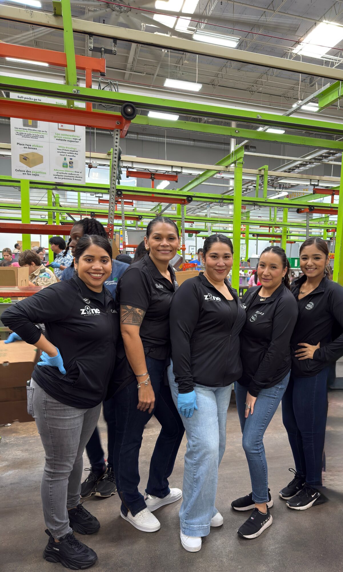 Five women standing together in a store, smiling, with green and orange shelves in the background.