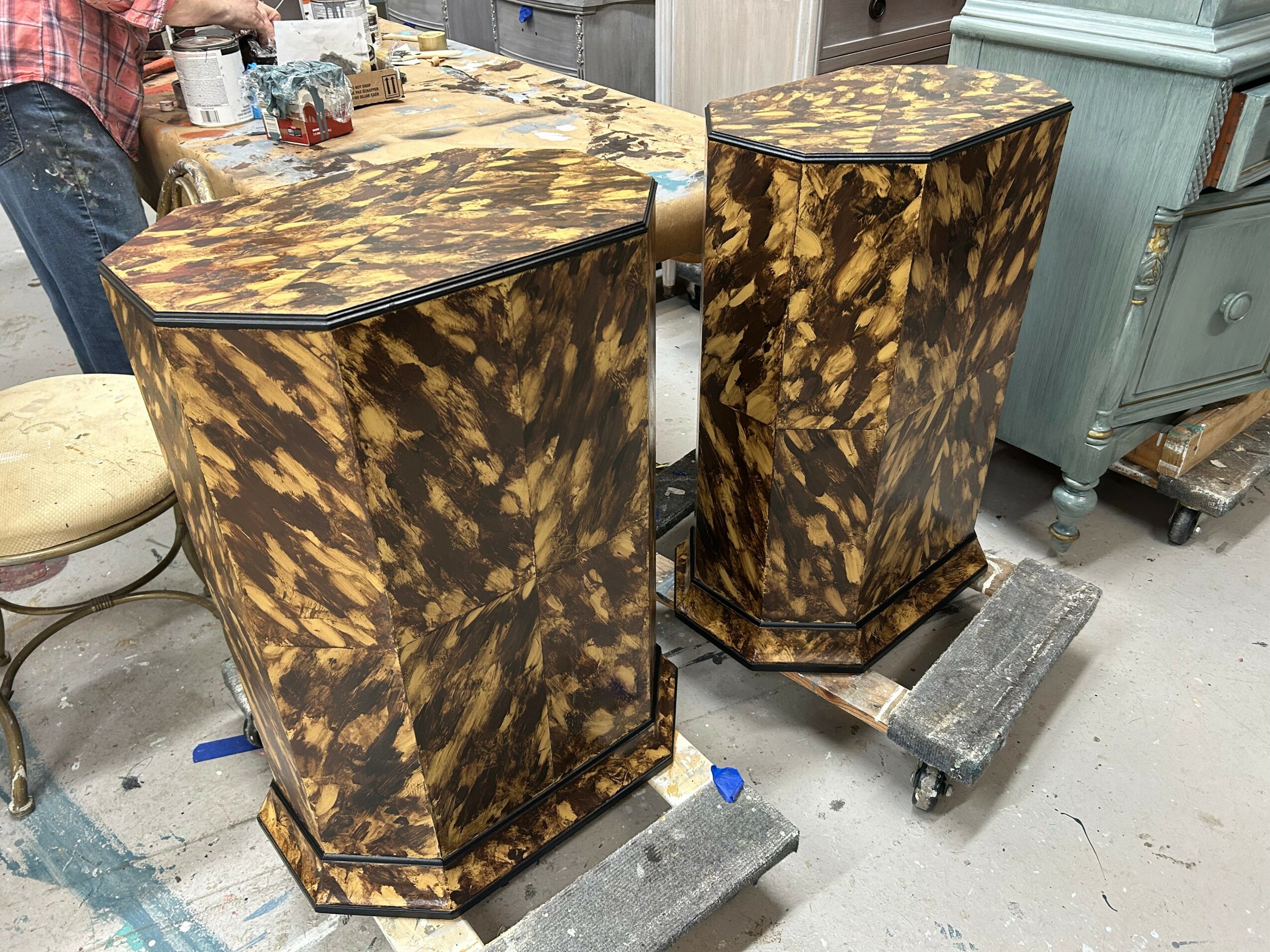 Two matching vintage-style cabinets with a tortoiseshell pattern, placed on dollies in a workshop or storage area.