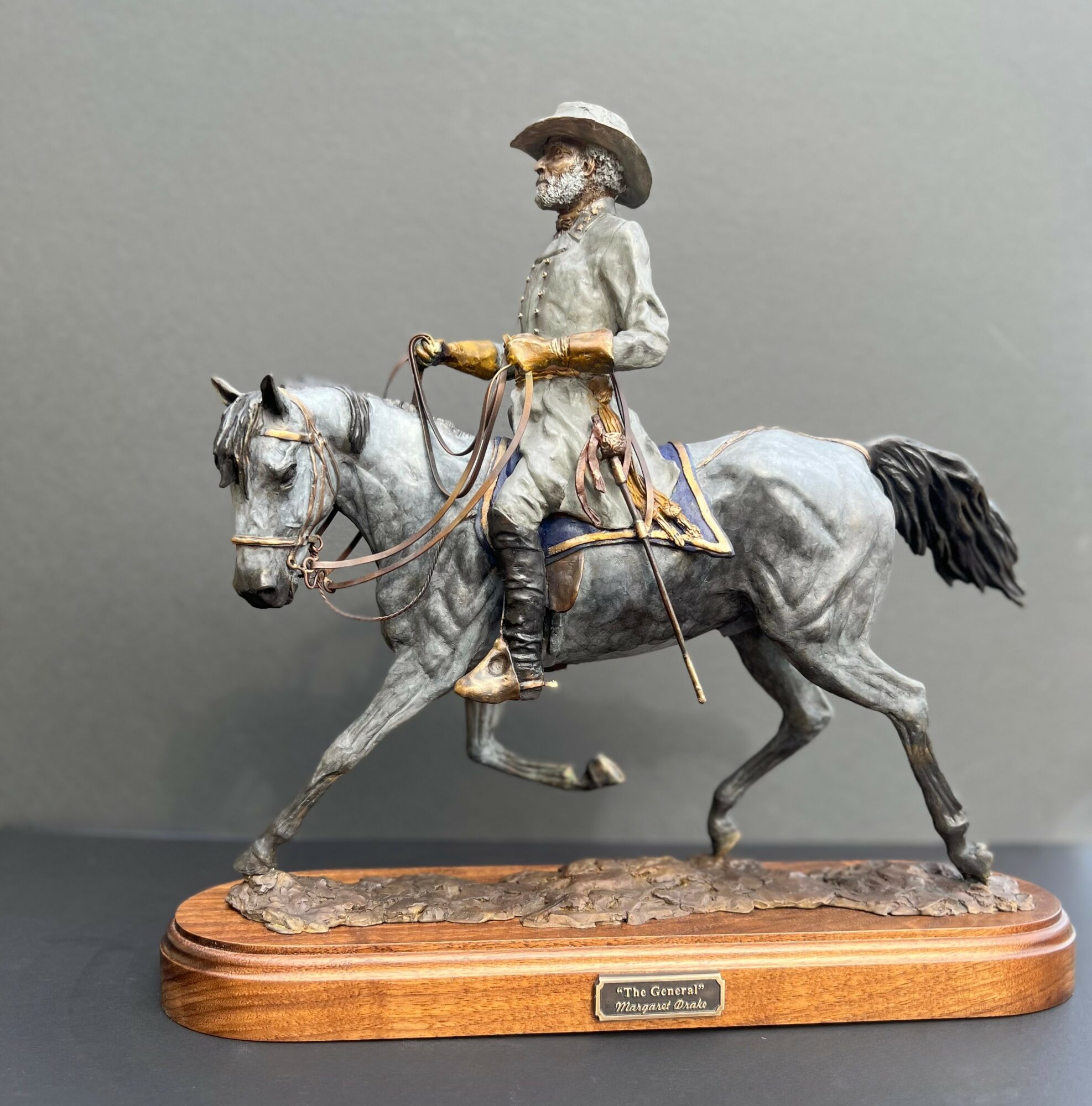 Statue of a man riding a horse, mounted on a wooden base with a plaque, against a plain background.
