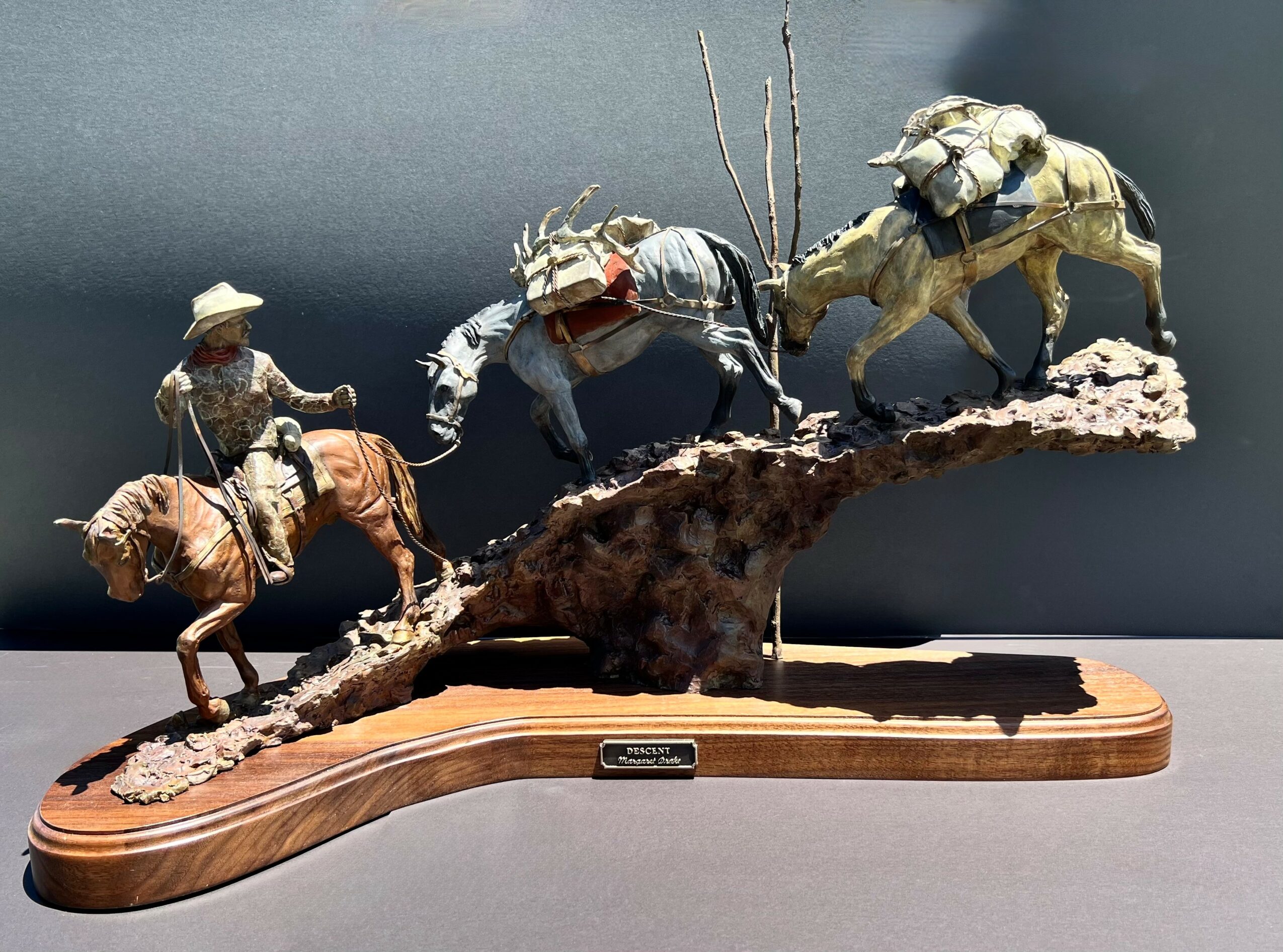 Group of four insect-like figures on a branch, mounted on a wooden base, with a dark background.