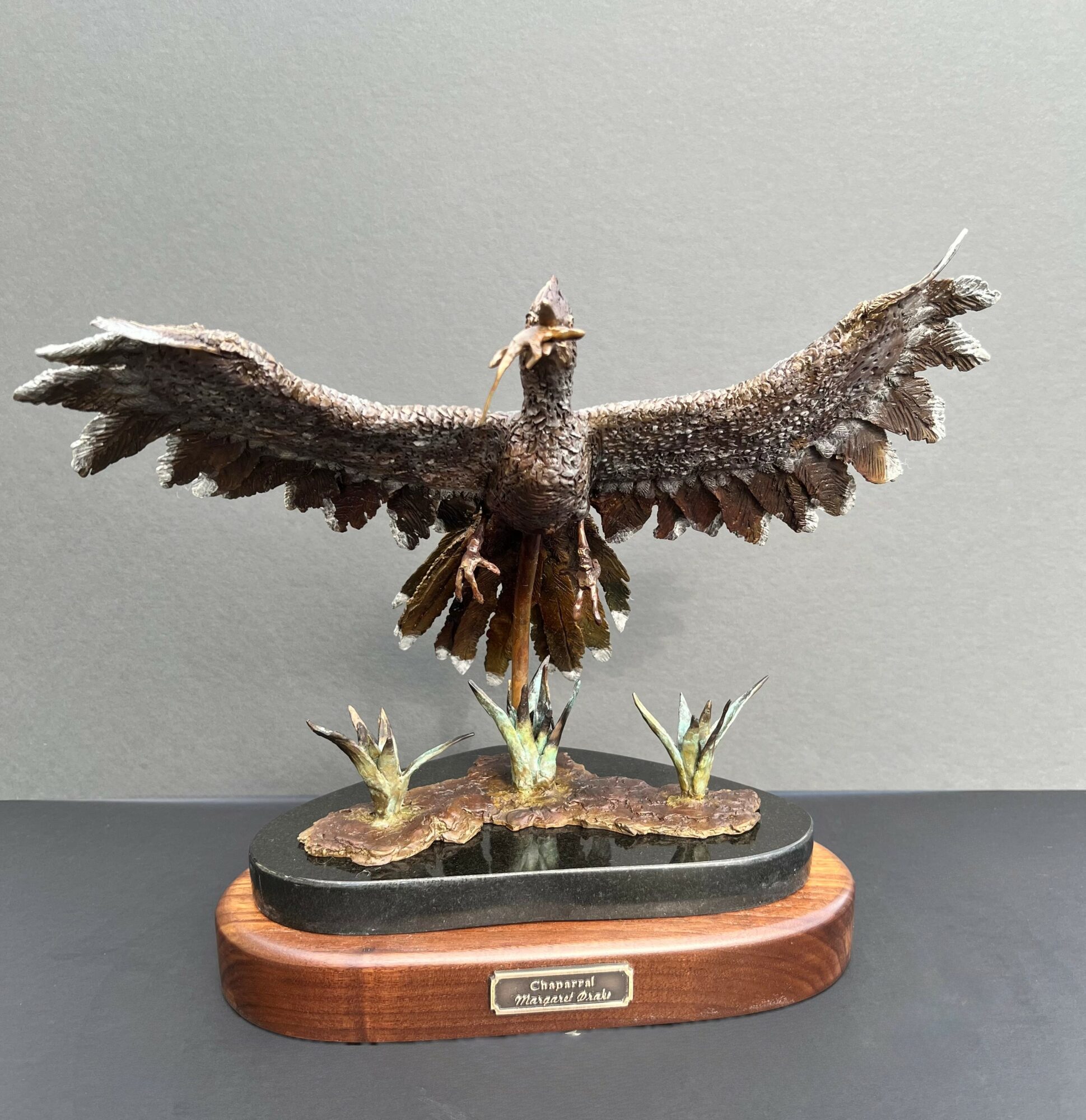 A detailed sculpture of a bird with wings spread wide, perched on a base with plants, mounted on a wooden stand.