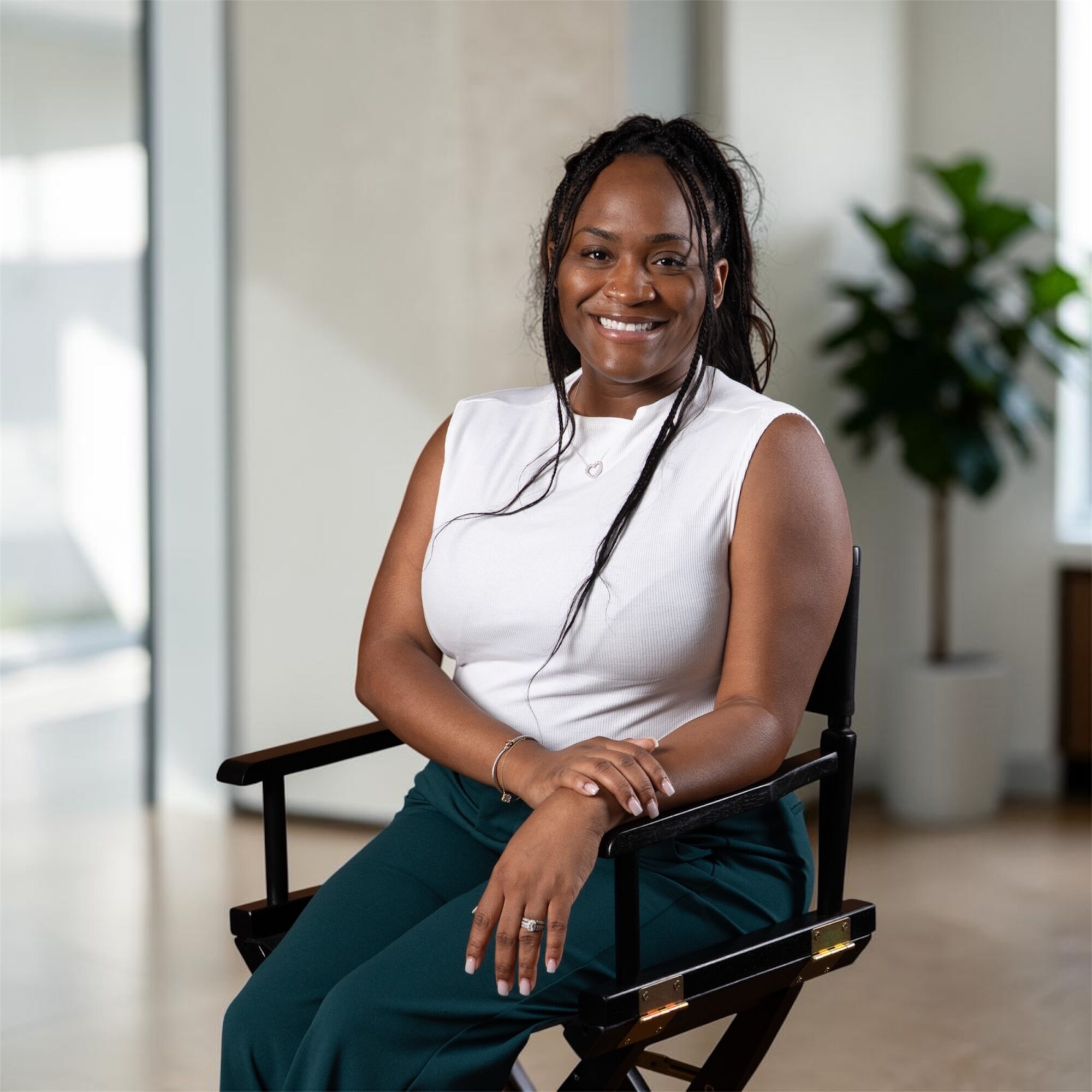 Smiling woman sitting on a chair indoors with a plant in the background.