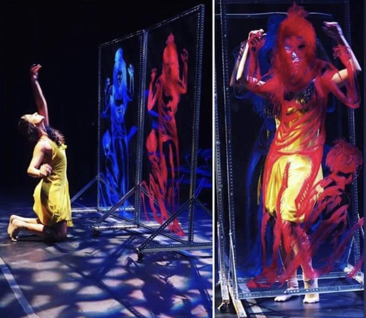 Person kneeling and looking at colorful reflections in mirrors, with shadows on the floor, in a dark setting.