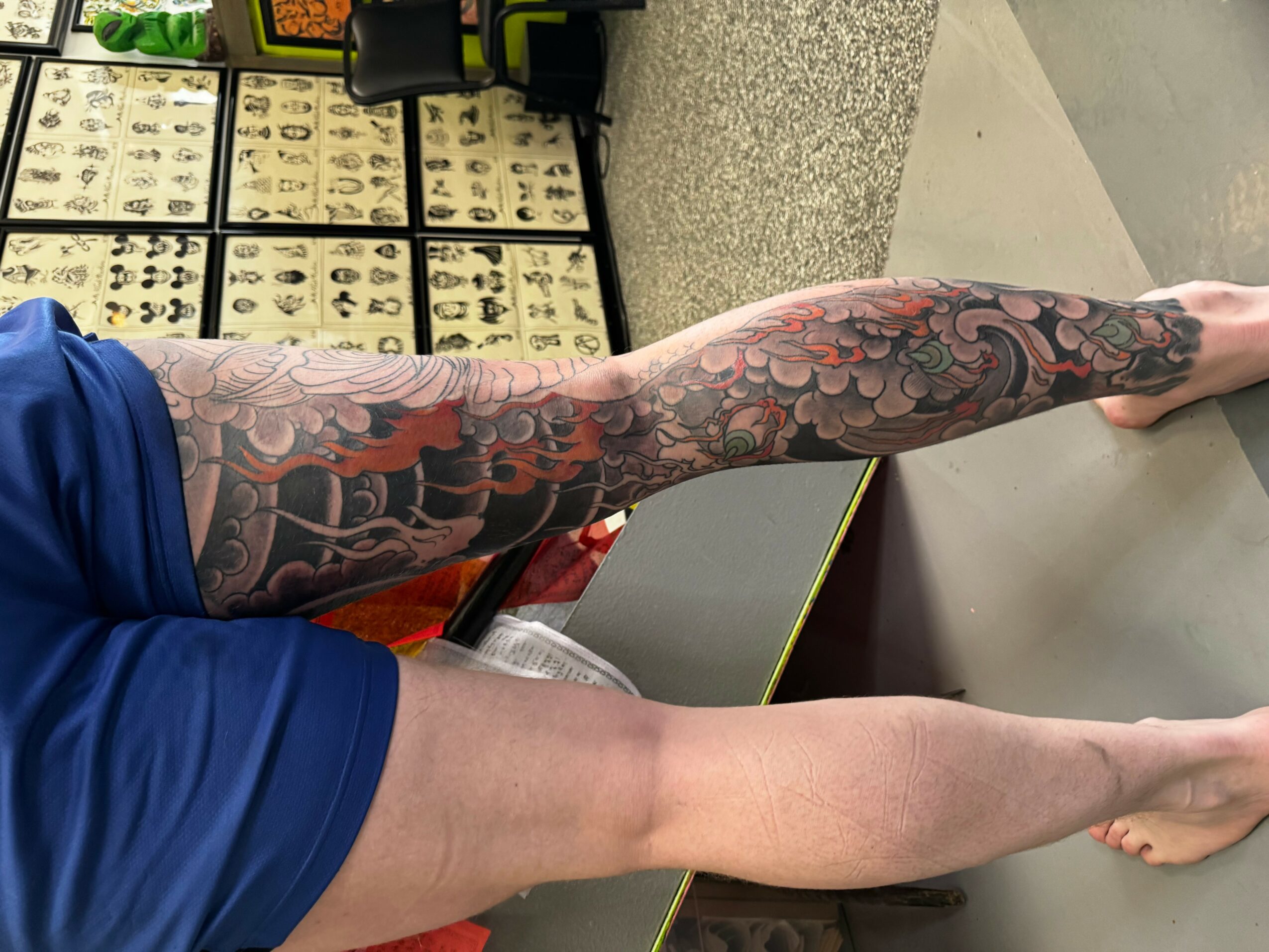 Person's tattooed arm and leg visible, with tattoo featuring floral and abstract designs, in a room with display cases.
